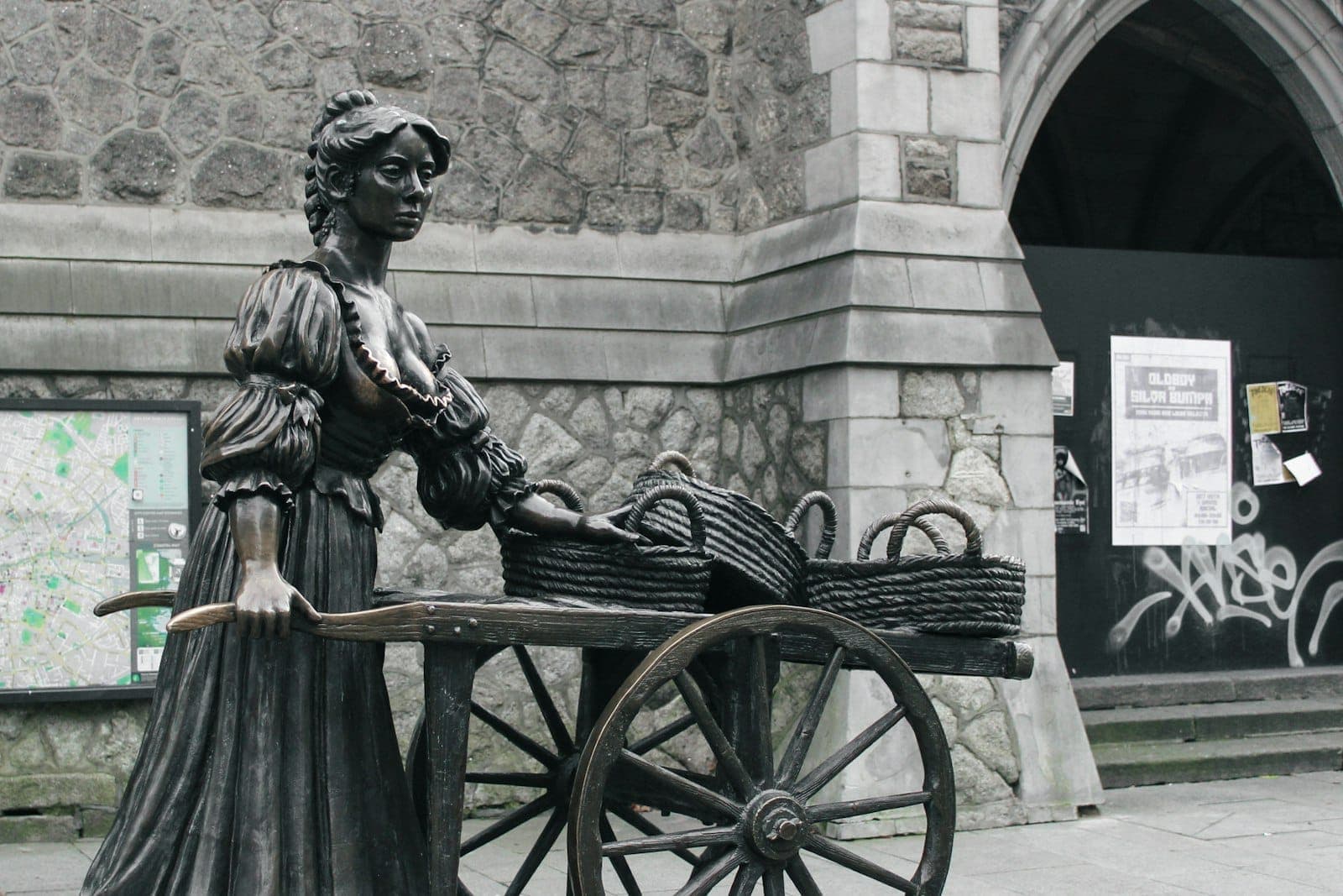 Suffolk Street'te bir taş binanın önünde arabasıyla duran bronz Molly Malone heykeli.