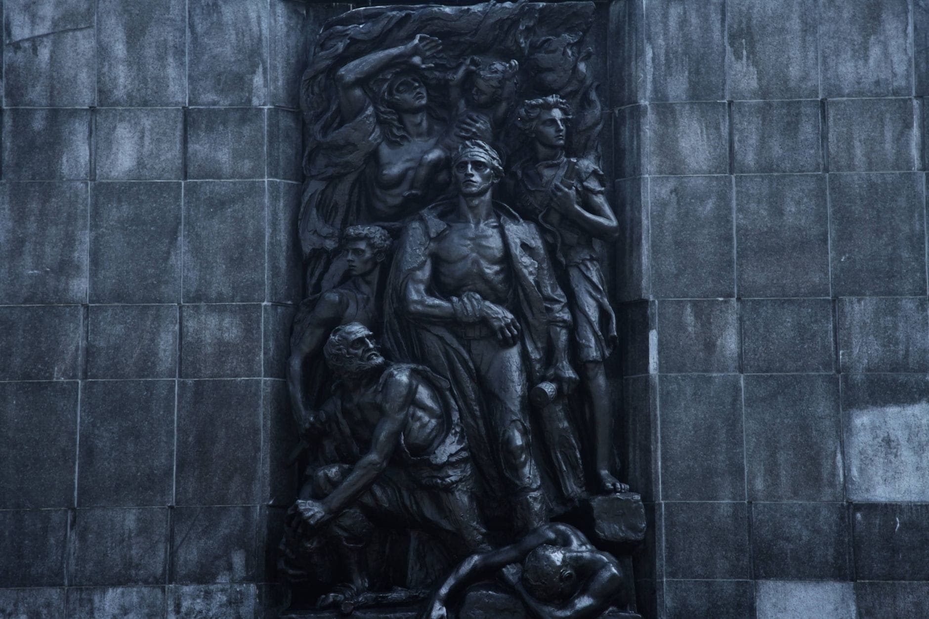 Nahaufnahme des eindrucksvollen Reliefs am Denkmal der Ghetto-Helden in Warschau: jüdische Kämpfer in bewegten Posen vor einer dunklen Steinwand.