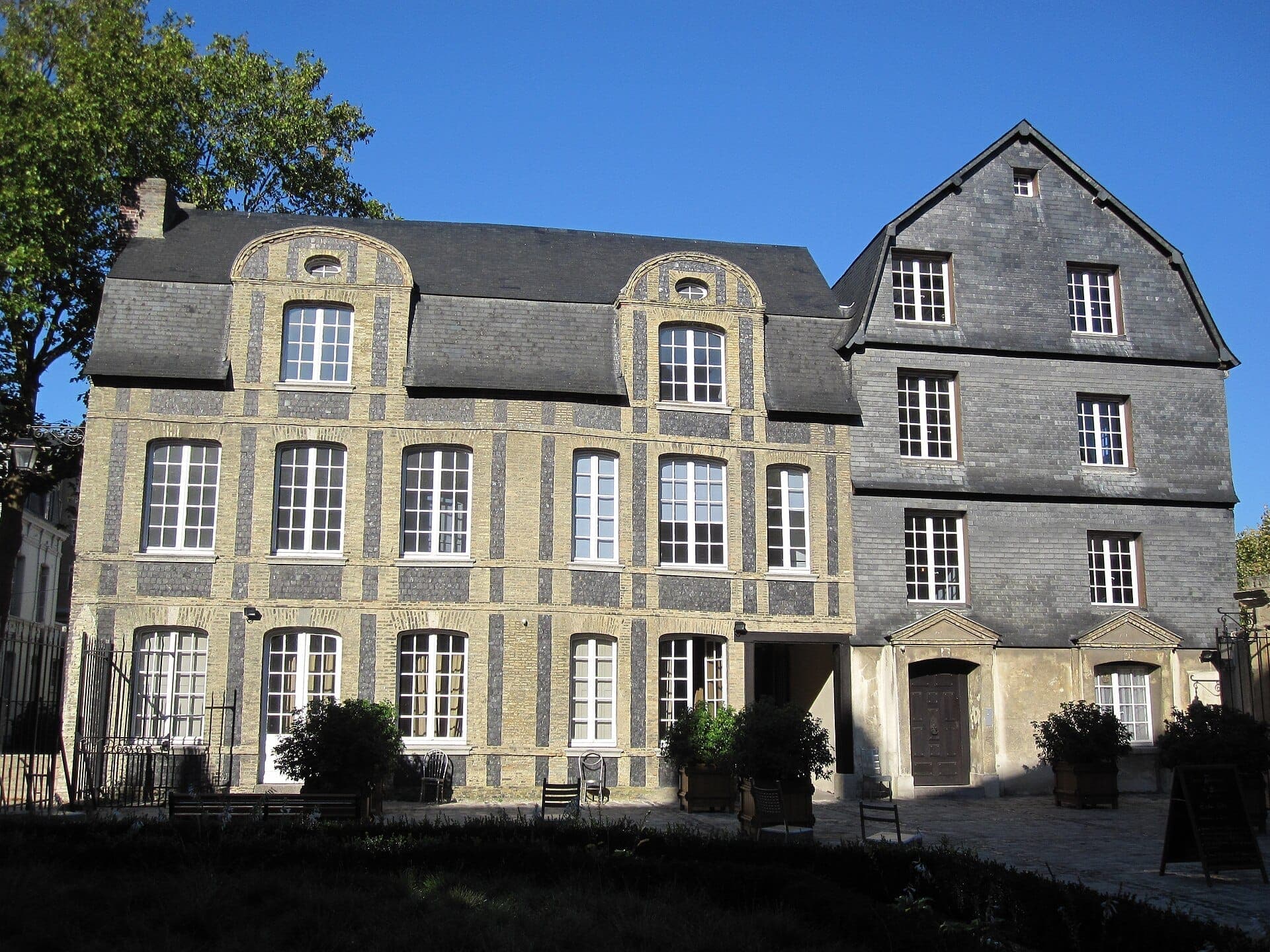 Nhìn từ phía trước của Musée de l'Ancien Havre tại Le Havre, với mặt tiền gạch vàng và đá phiến đặc trưng dưới bầu trời xanh trong.