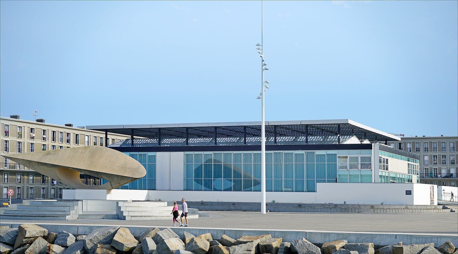 Cảnh ngoại thất của Musée d'Art Moderne André Malraux tại Le Havre, nổi bật với mặt tiền kính, tác phẩm điêu khắc hiện đại và đại lộ rộng rãi dưới bầu trời trong xanh.