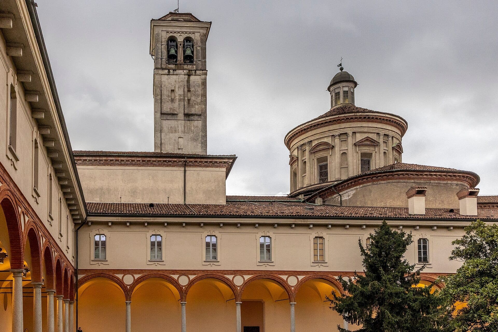 Exterior view of Museo Nazionale della Scienza e della Tecnologia Leonardo da Vinci, showcasing cloister arches and historic monastery architecture under a cloudy sky.