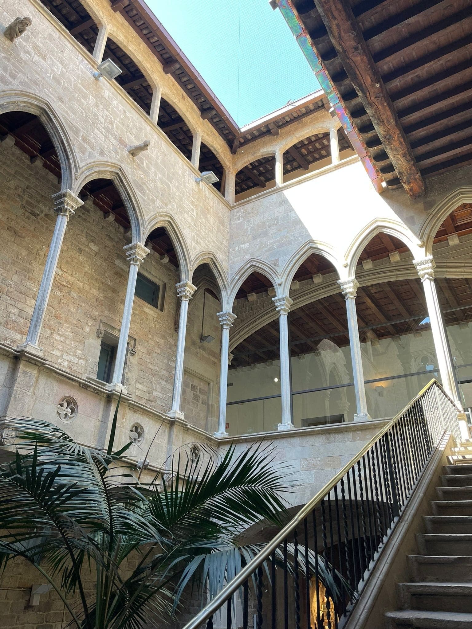 Sân đá của Museu Picasso Barcelona với những cửa sổ hình vòm, cây cọ và cầu thang dưới ánh sáng tự nhiên ban ngày.