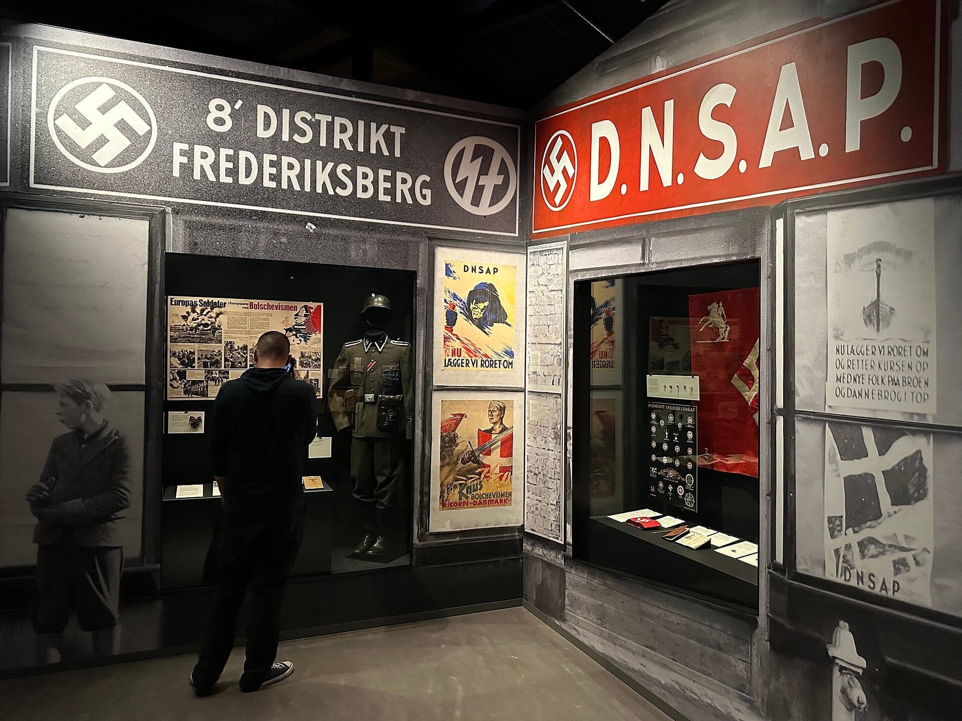 Ein Besucher studiert Ausstellungsstücke aus dem Zweiten Weltkrieg und Nazi-Memorabilia im Museum of Danish Resistance in Kopenhagen, umgeben von historischen Plakaten und Uniformen.