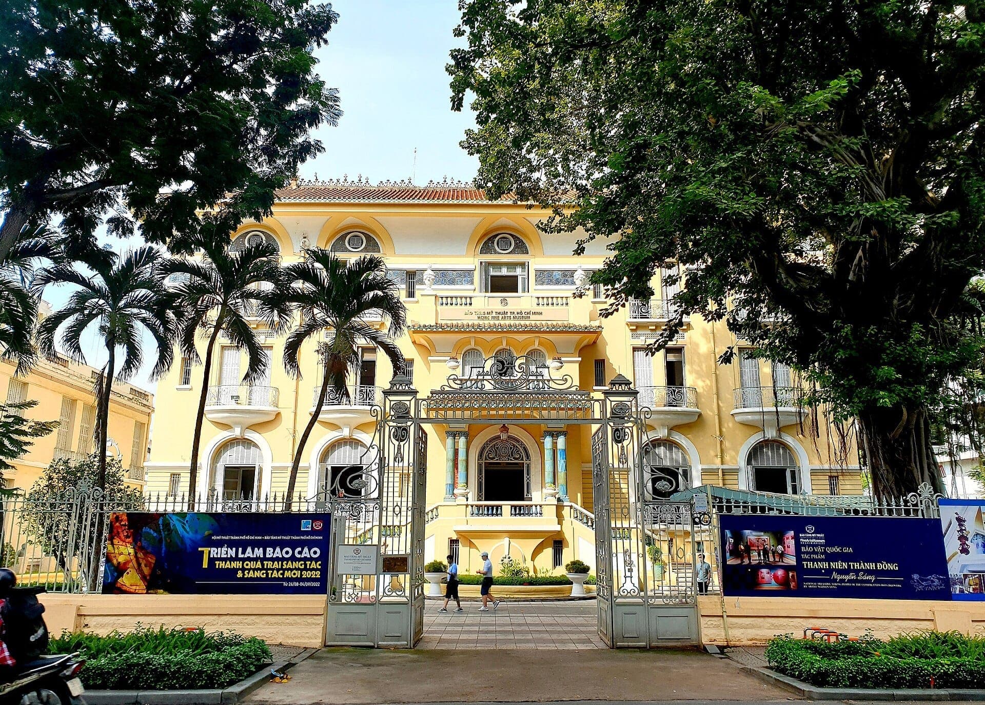 Bảo tàng Mỹ thuật Thành phố Hồ Chí Minh với mặt tiền màu vàng phong cách thuộc địa Pháp, cổng sắt chạm trổ tinh xảo và những cây cọ nhiệt đới phía trước.