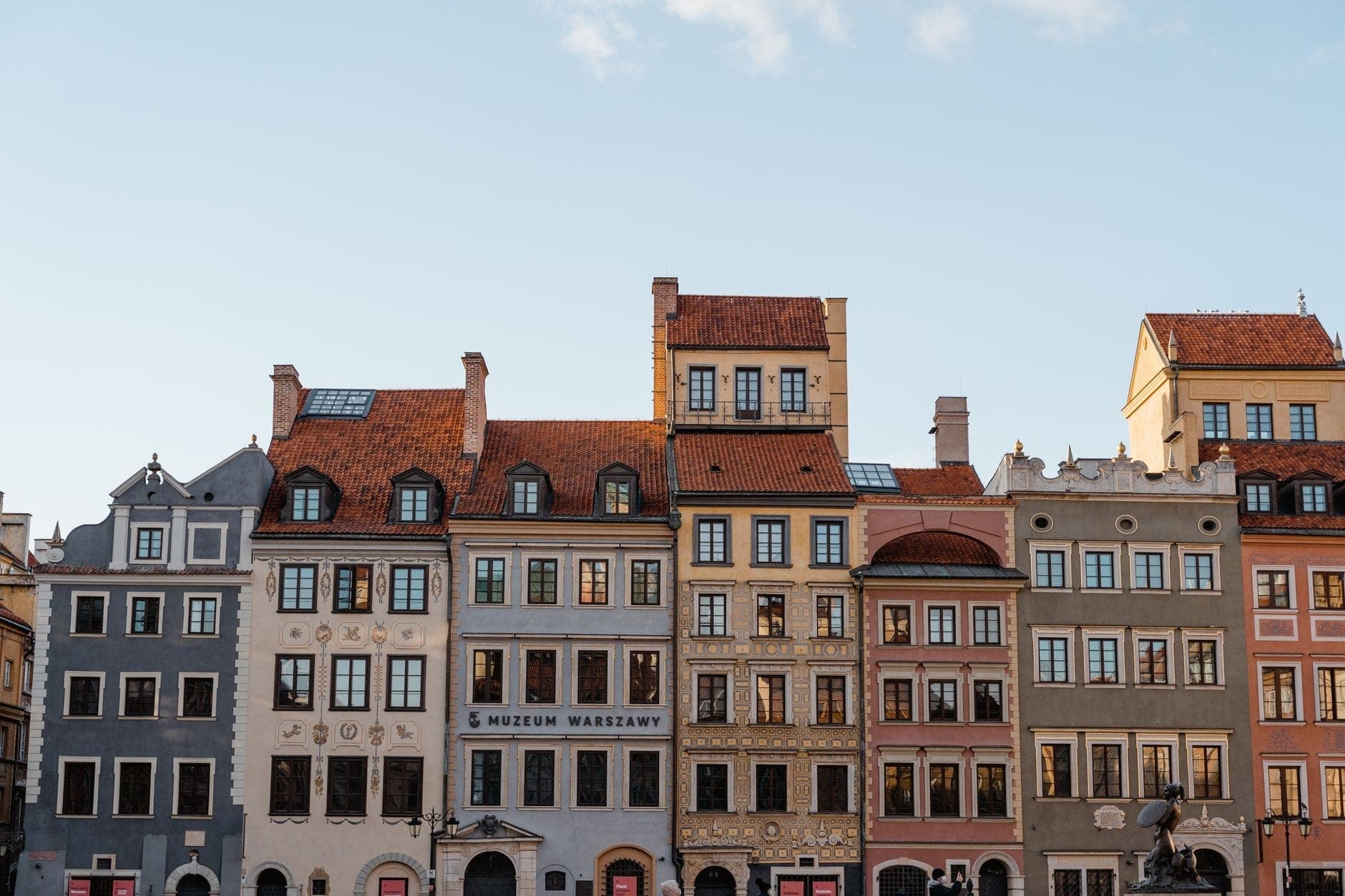 Eine Reihe bunter rekonstruierter Bürgerhäuser am Altstadtmarktplatz in Warschau, mit dem Museum of Warsaw prominent in der Mitte, unter einem klaren Himmel.