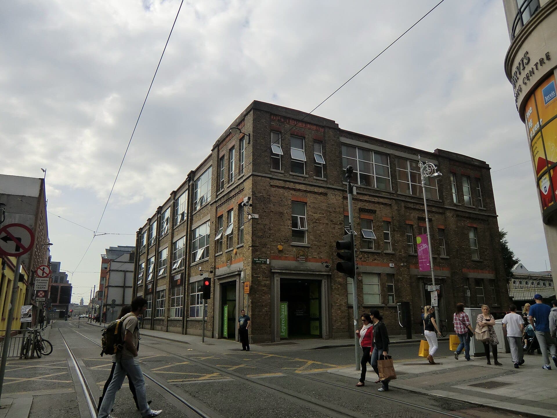 Straßenansicht des Gebäudes des National Leprechaun Museum in Dublin, mit Menschen, die an einer Stadtkreuzung an einem bewölkten Tag die Straße überqueren.