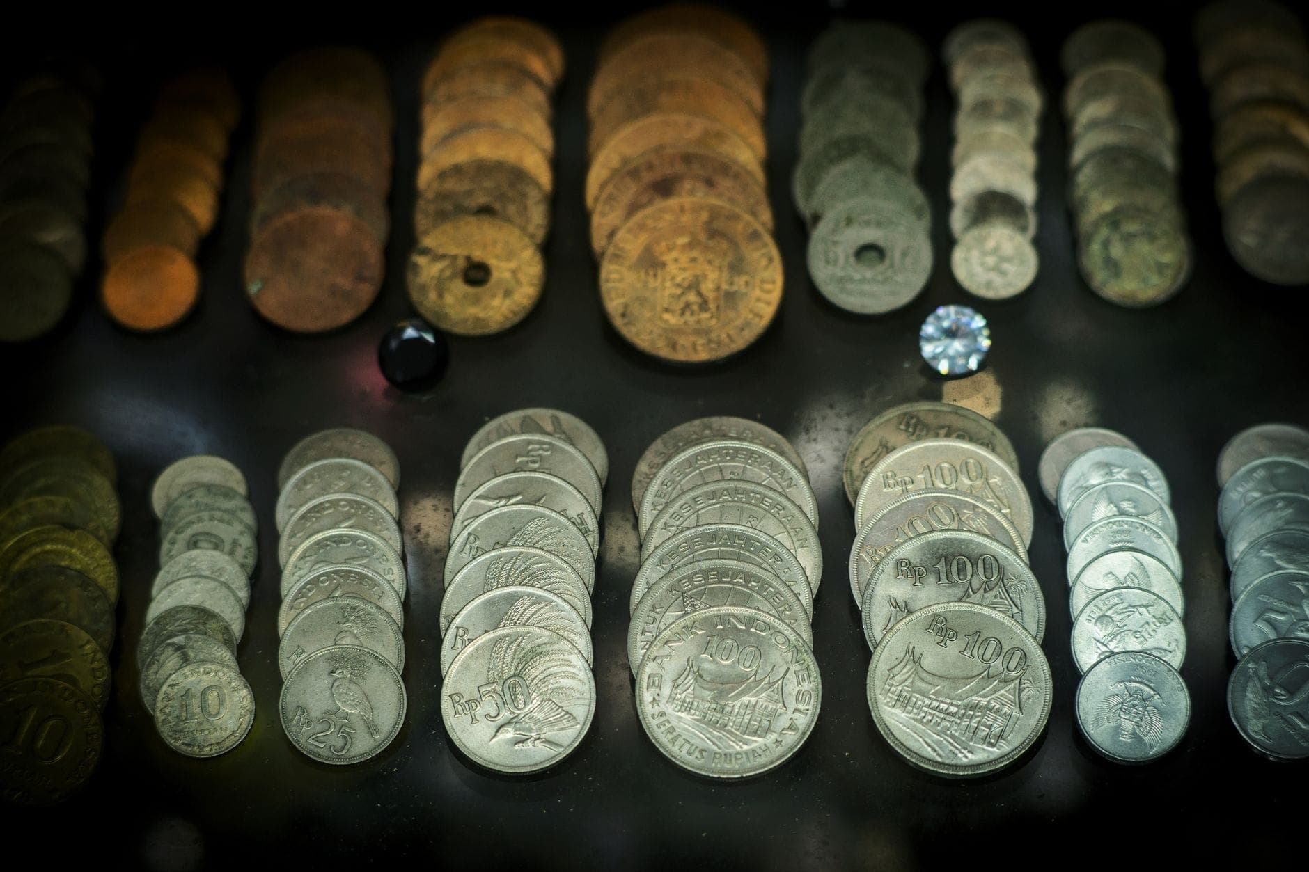 Rows of ancient and modern coins displayed in a museum case on a dark background, showcasing the variety and history of currency in Athens.