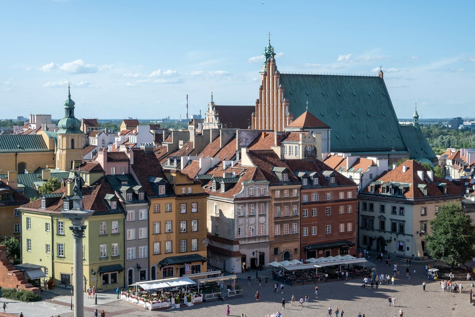 Panoramablick auf die bunten Bürgerhäuser des Warschauer Altstadtmarkts mit der Erzkathedrale St. Johannes und historischen Gebäuden unter strahlend blauem Himmel.