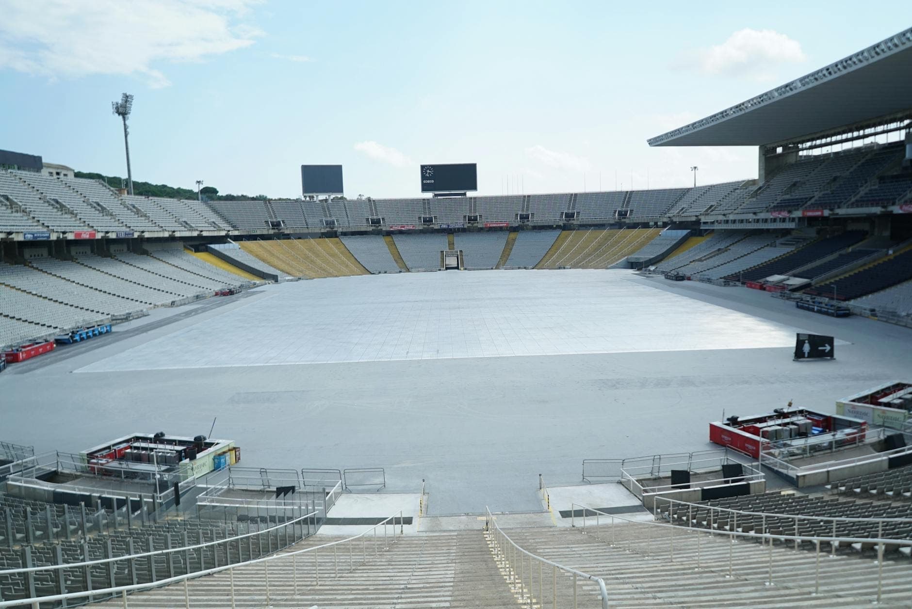 Toàn cảnh sân vận động Estadi Olímpic Lluís Companys ở Barcelona với khán đài trống, bầu trời rộng mở và một phần đường chạy điền kinh, gợi lên di sản Olympic lịch sử.