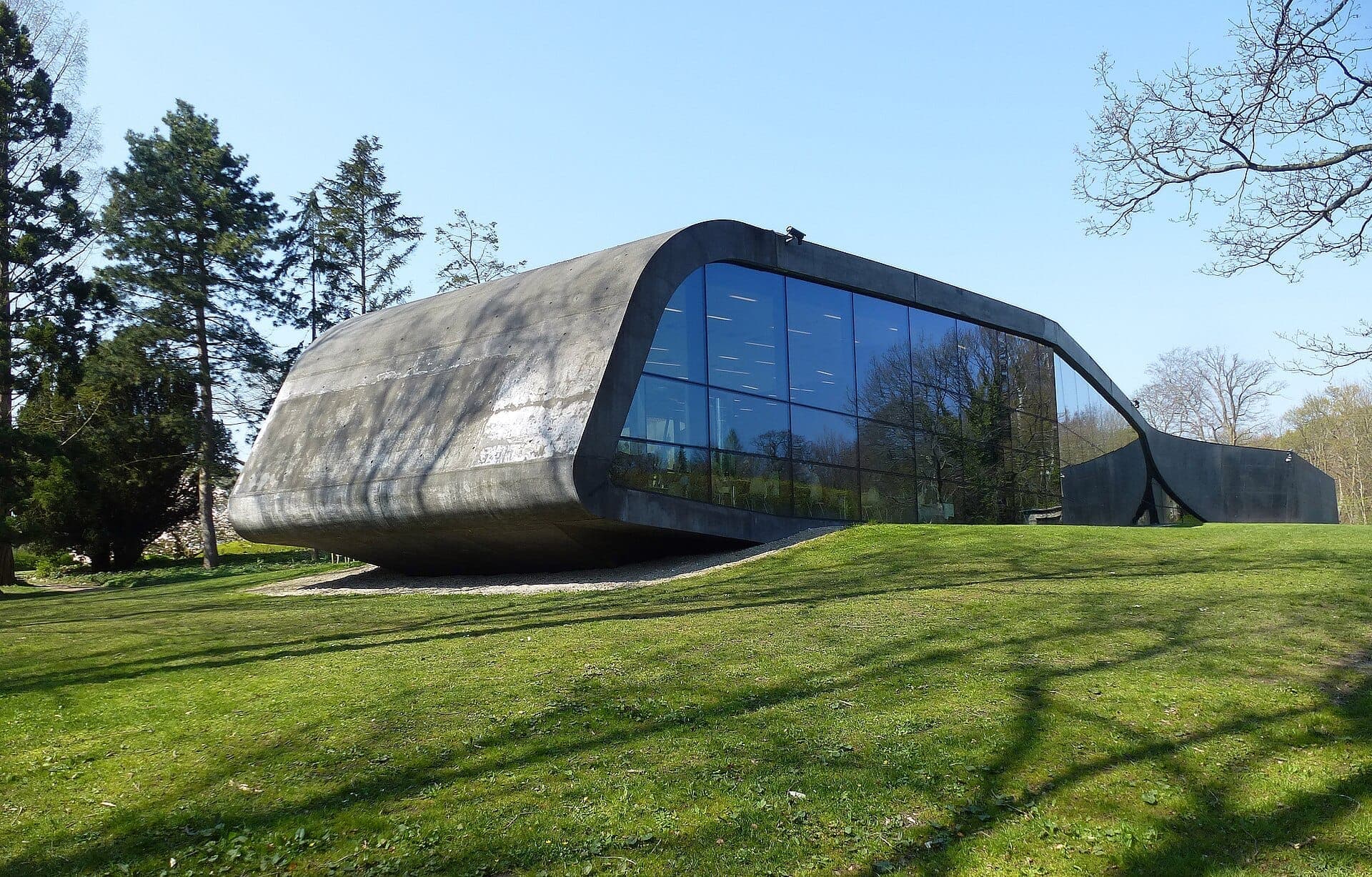 Moderne, von Zaha Hadid entworfene Erweiterung des Ordrupgaard Museums in Kopenhagen mit geschwungener Beton- und Glasfassade, umgeben von grünem Rasen und Bäumen.