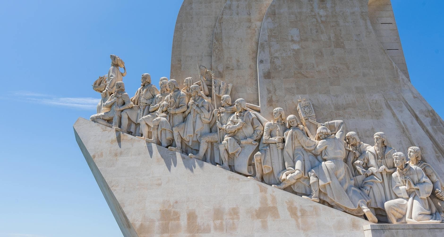 Góc chụp rộng của đài tưởng niệm Padrão dos Descobrimentos tại Lisbon, nổi bật với các tượng đá chạm khắc tinh xảo trên nền trời xanh, lý tưởng cho ảnh bìa điểm tham quan.