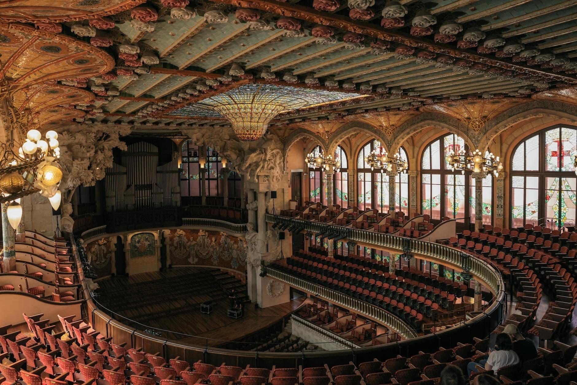 Góc rộng chụp sảnh hòa nhạc chính của Palau de la Música Catalana, nổi bật với mái vòm kính màu tráng lệ, cửa sổ vòm, ban công tinh xảo và hàng ghế đỏ trải dài.