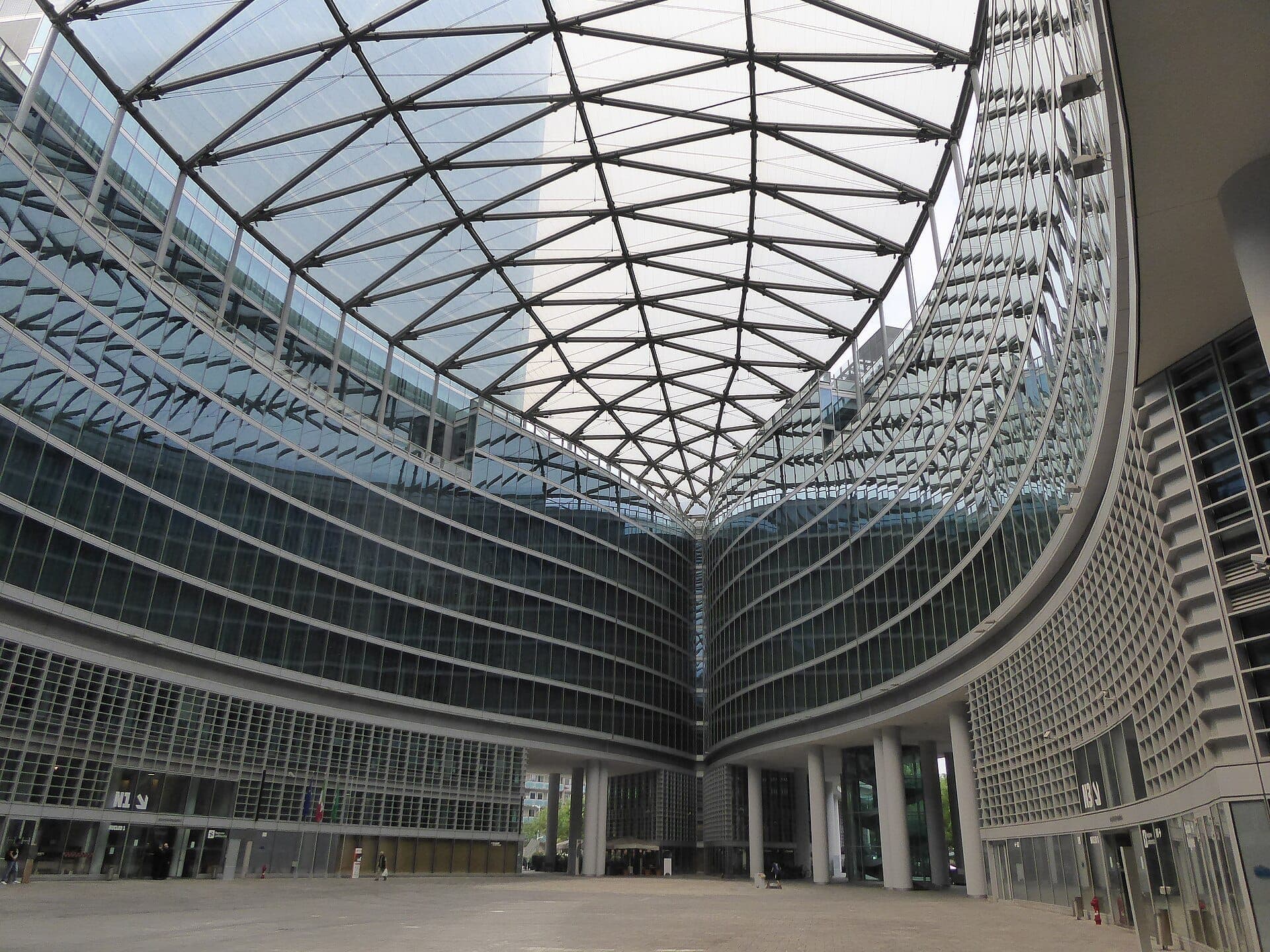 View of Palazzo Lombardia’s modern glass façade and expansive open piazza, with angular steel roof structure, in Milan’s Porta Nuova district.