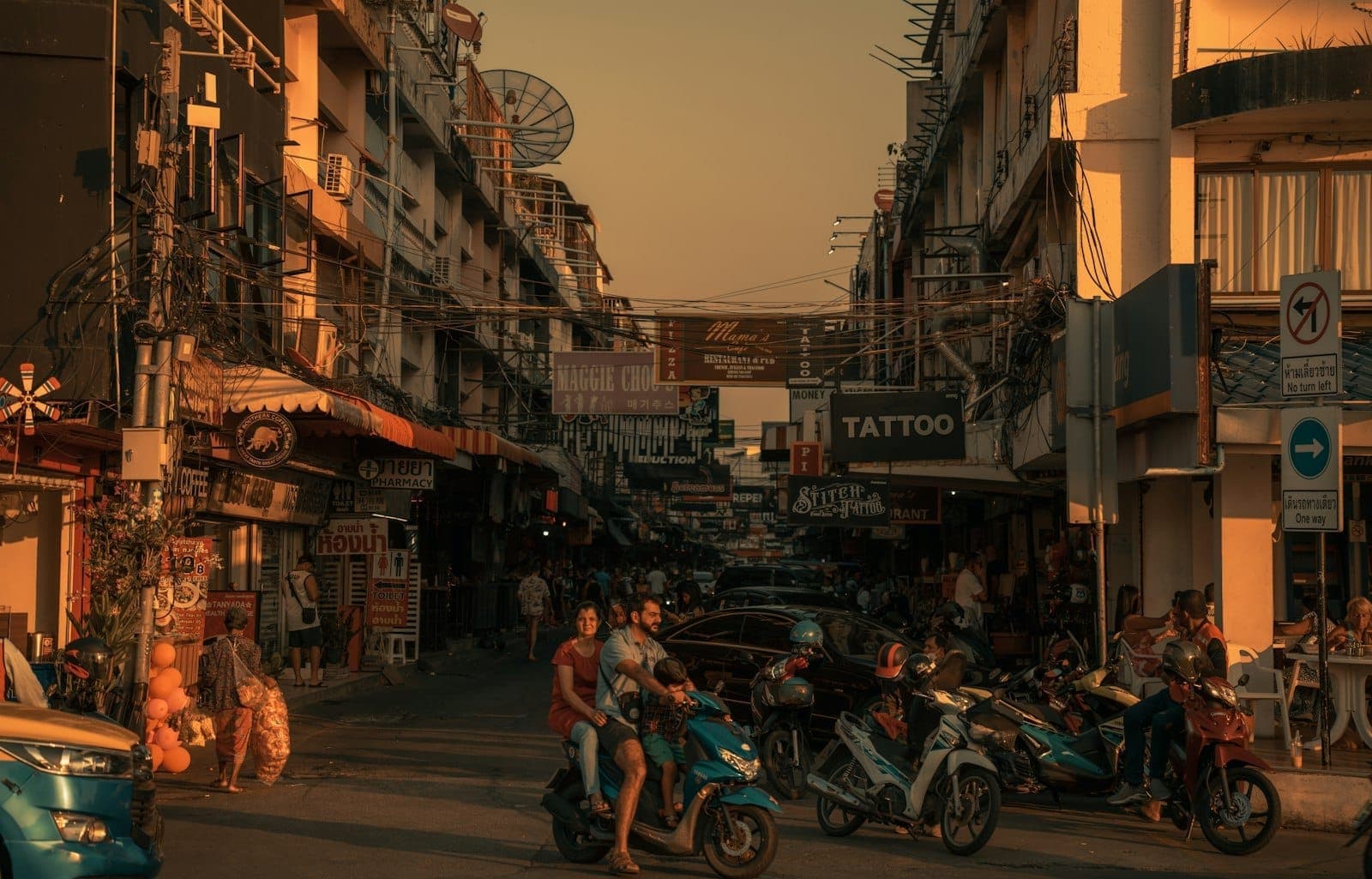 Busy street scene at dusk in Pattaya with small bars, motorcycles, and people, showing a more local nightlife area.