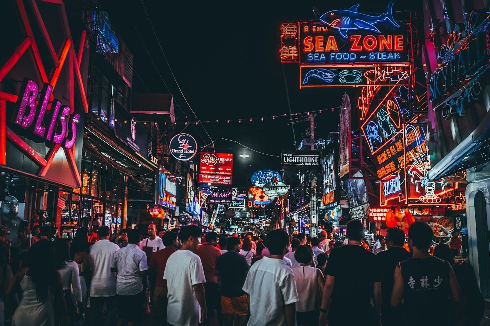 Crowd of people walking through Pattaya's vibrant Walking Street at night, surrounded by colorful neon club and bar signs, capturing the city's energetic nightlife.
