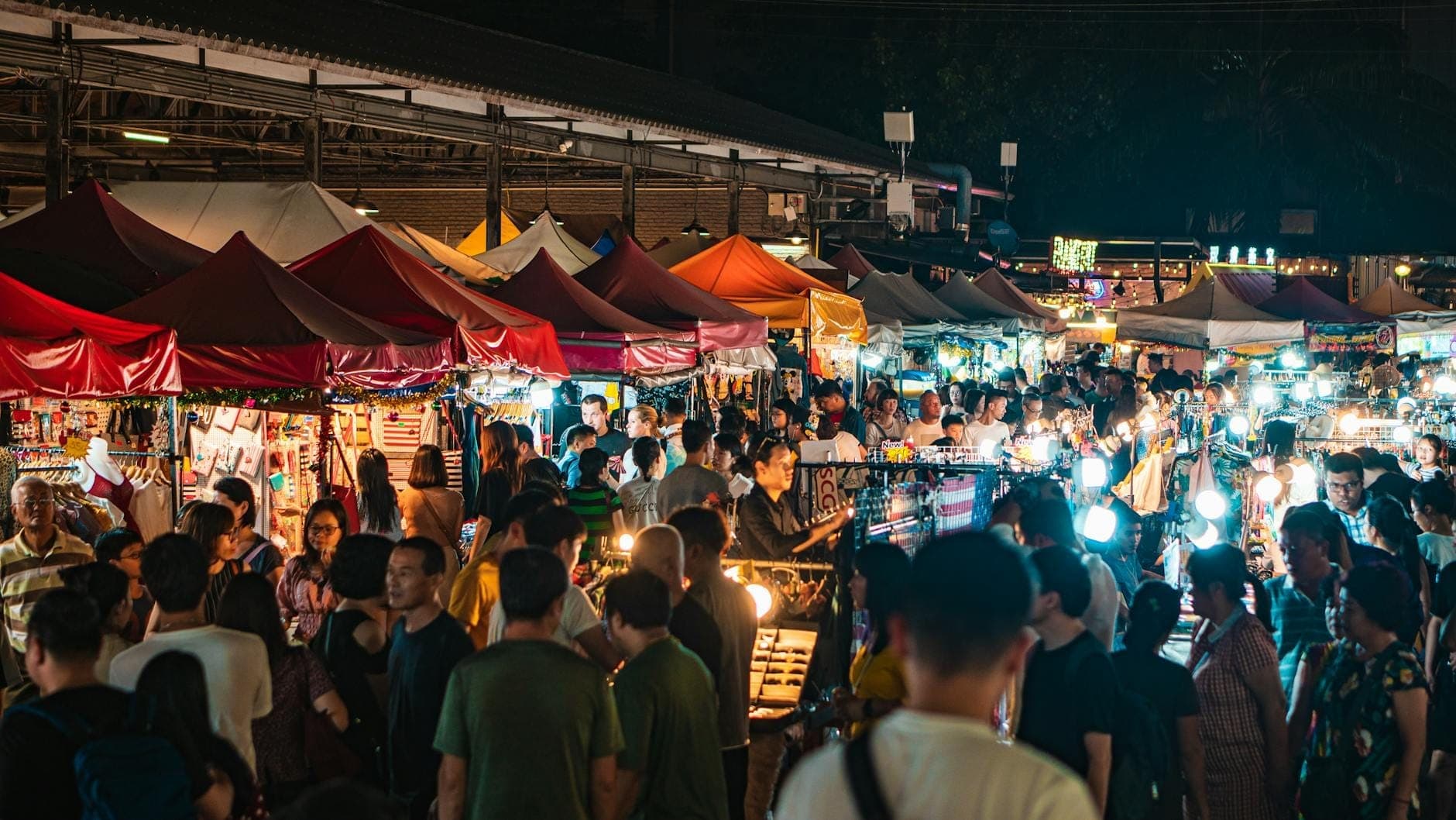 Crowds explore Pattaya Park Night Market at night, browsing stalls under colorful tents with bright lights and local vendors visible.