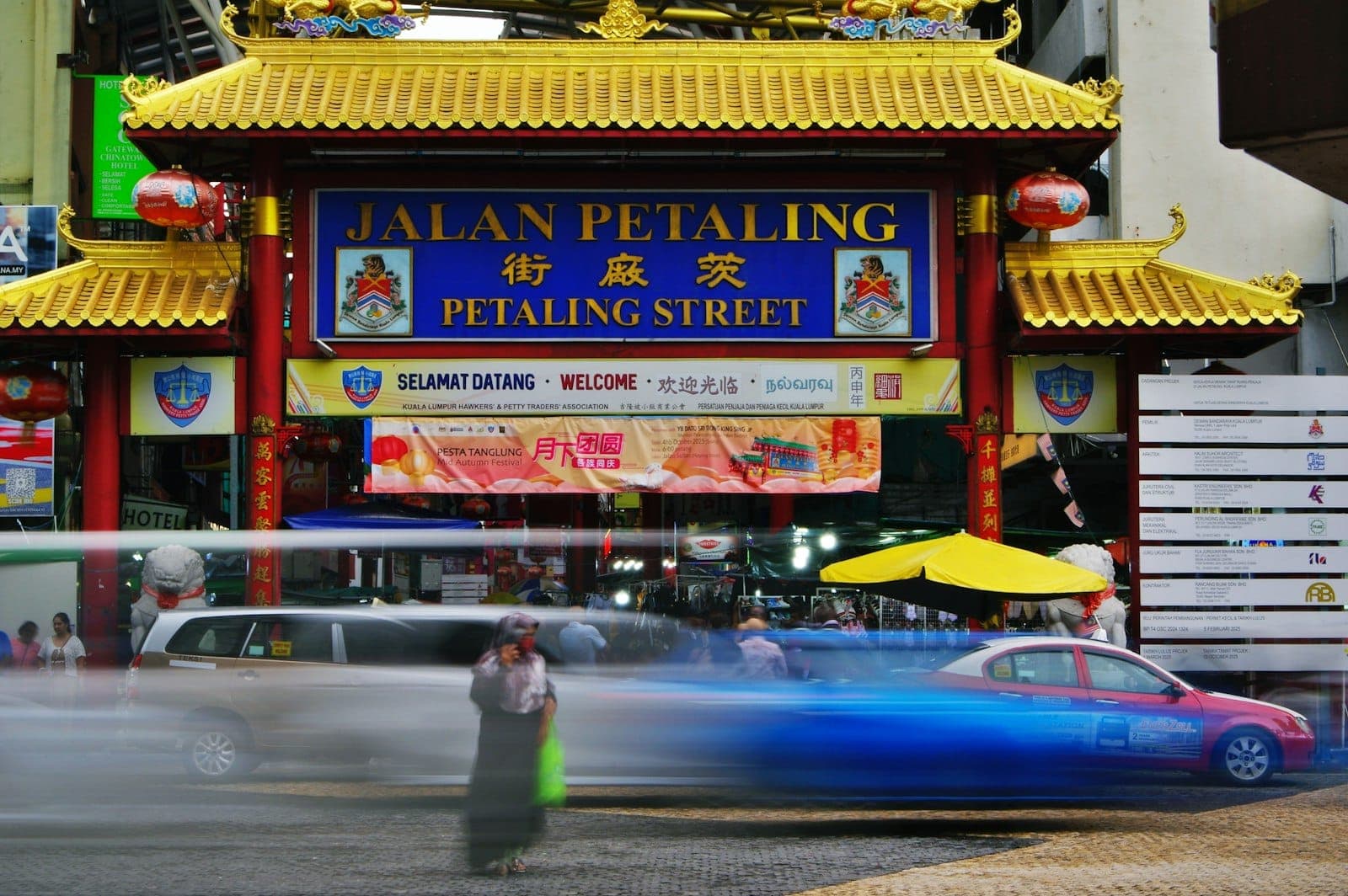 Lối vào nhộn nhịp của chợ Petaling Street tại khu phố Tàu Kuala Lumpur, đóng khung bởi đèn lồng đỏ và vòm gạch.