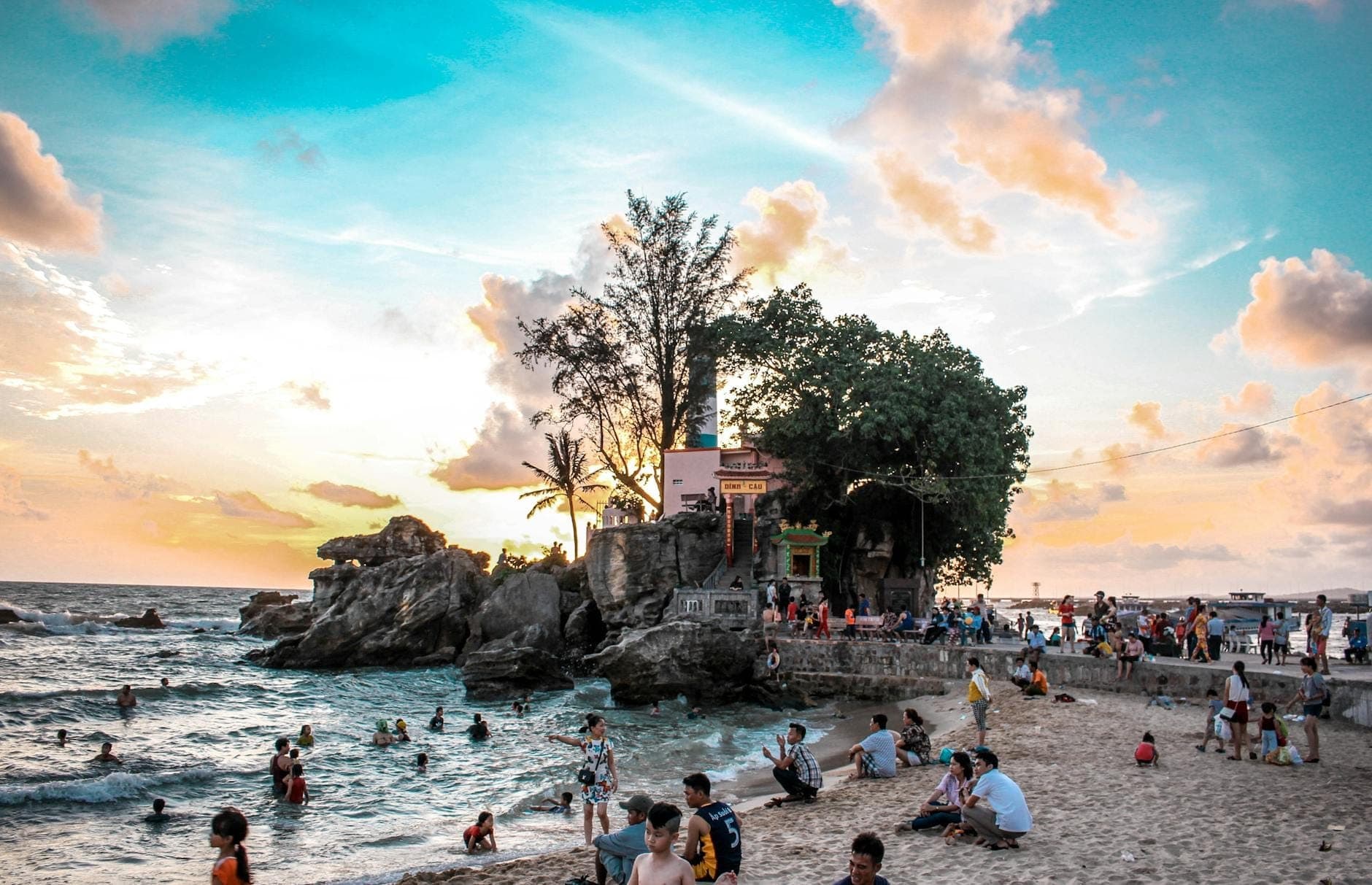 Bãi biển Phú Quốc lúc hoàng hôn với người tắm biển, bờ đá và ngôi đền ven biển