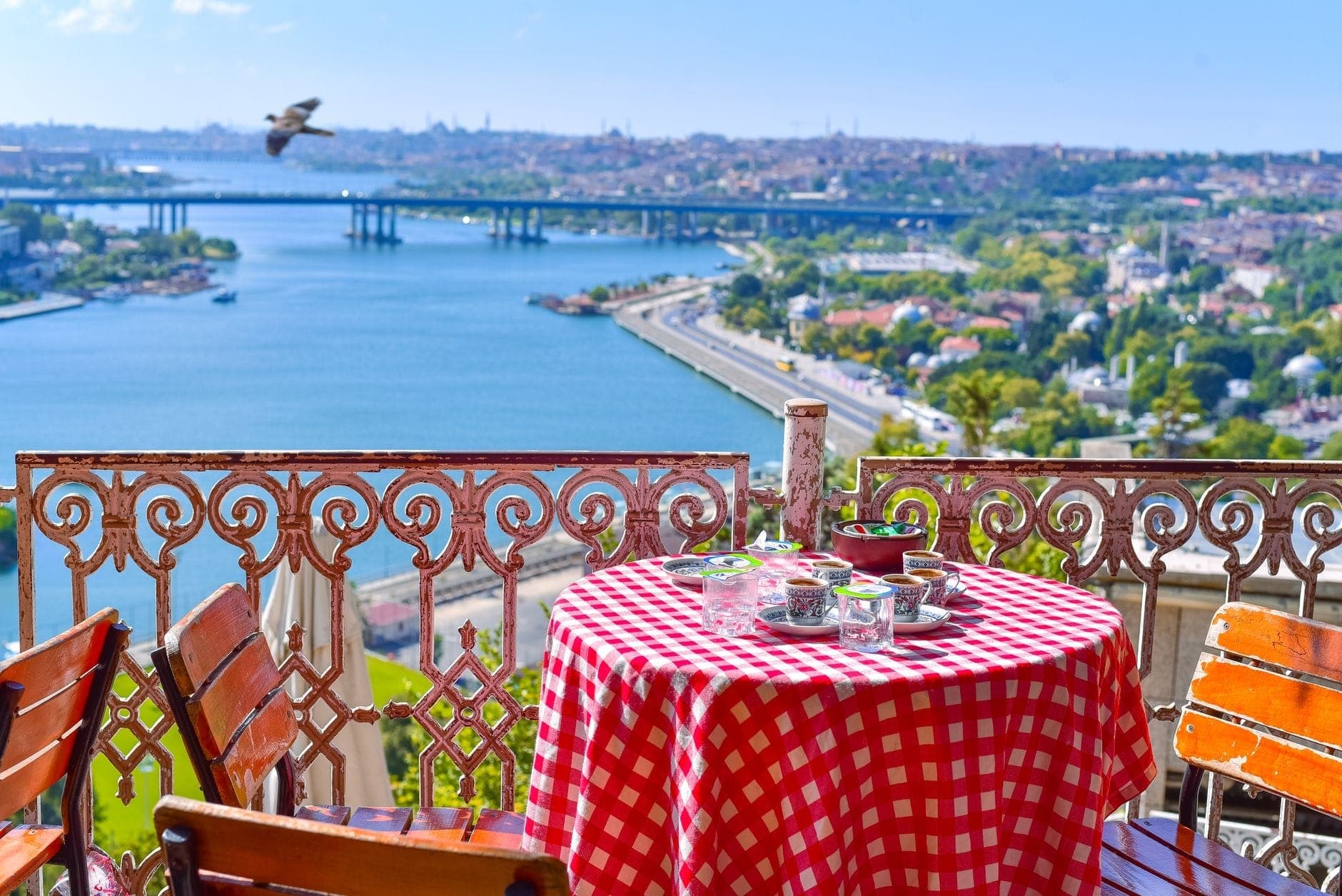 Tisch mit rot-weiß karierter Tischdecke für den Tee gedeckt im Pierre-Loti-Café, mit Blick auf das Goldene Horn und die Stadtsilhouette Istanbuls an einem klaren Tag.