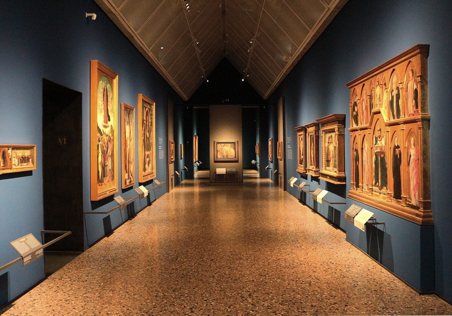 Wide view of a gallery room in the Pinacoteca di Brera, Milan, with Renaissance paintings displayed on deep blue walls under soft lighting.