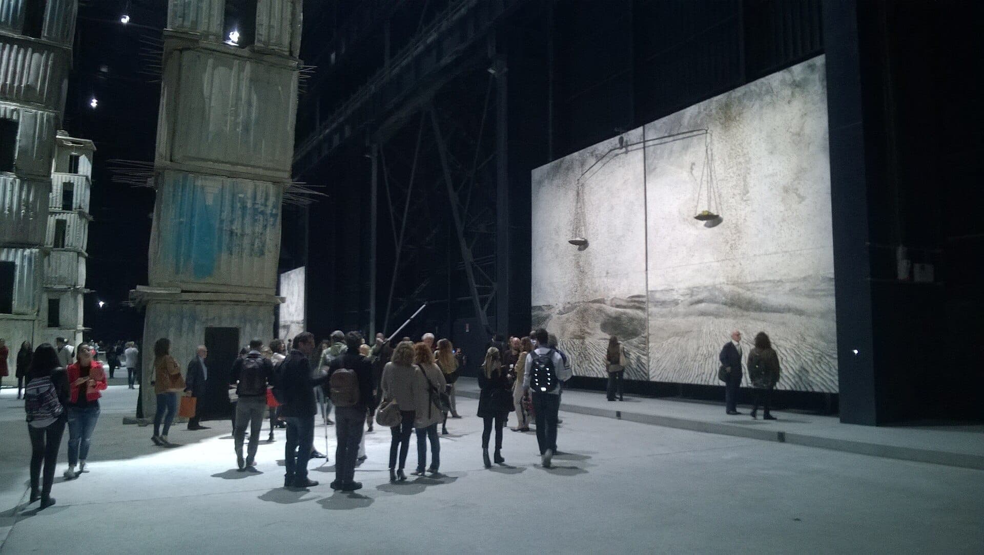Visitors explore large contemporary art installations inside the expansive industrial space of Pirelli HangarBicocca in Milan, featuring towering structures and wall-sized artwork.
