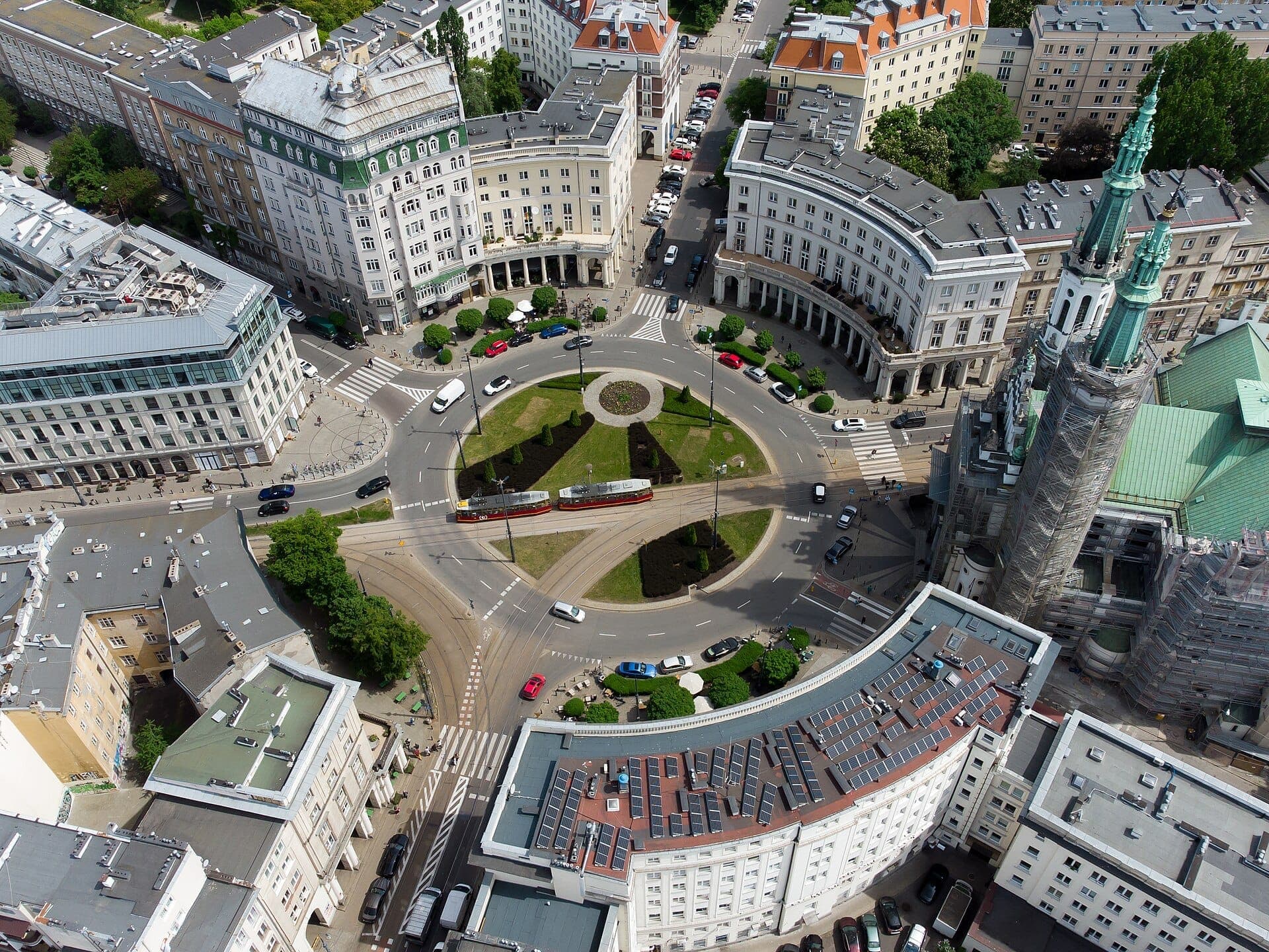 Luftaufnahme des Plac Zbawiciela in Warschau mit dem kreisförmigen Kreisverkehr, den umliegenden historischen Gebäuden, der Straßenbahnlinie und der grünen Mittelinsel.