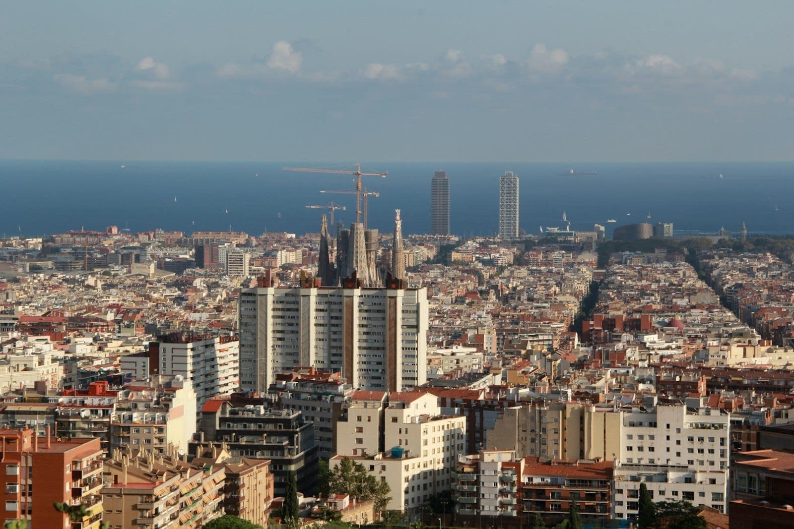 Panoramikong tanawin ng Poblenou at Olympic Village ng Barcelona kasama ang dalawang tore, grid ng lungsod, at Dagat Mediteraneo sa ilalim ng maliwanag na asul na langit.