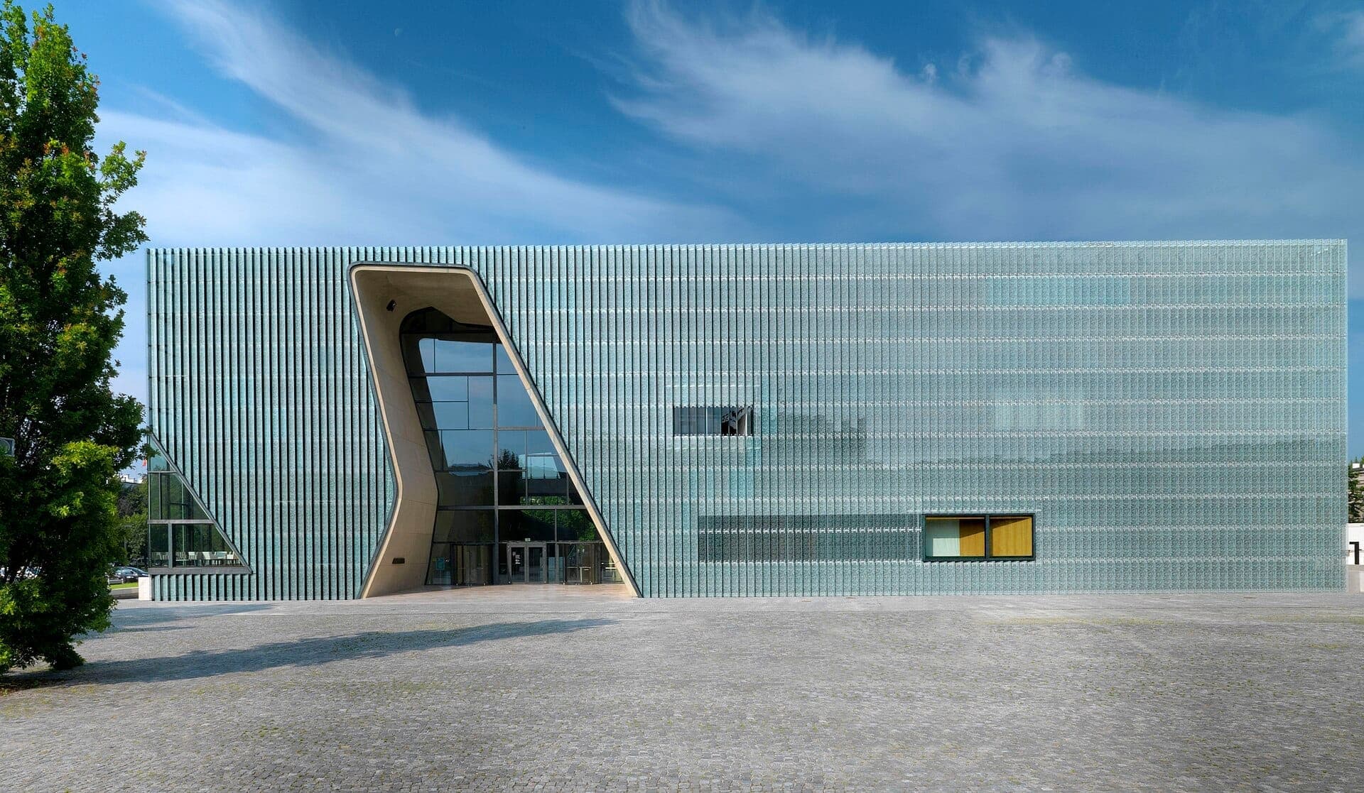 Moderne Glasfassade des POLIN Museums der Geschichte der polnischen Juden mit geometrischen Formen unter einem strahlend blauen Himmel in Warschau.