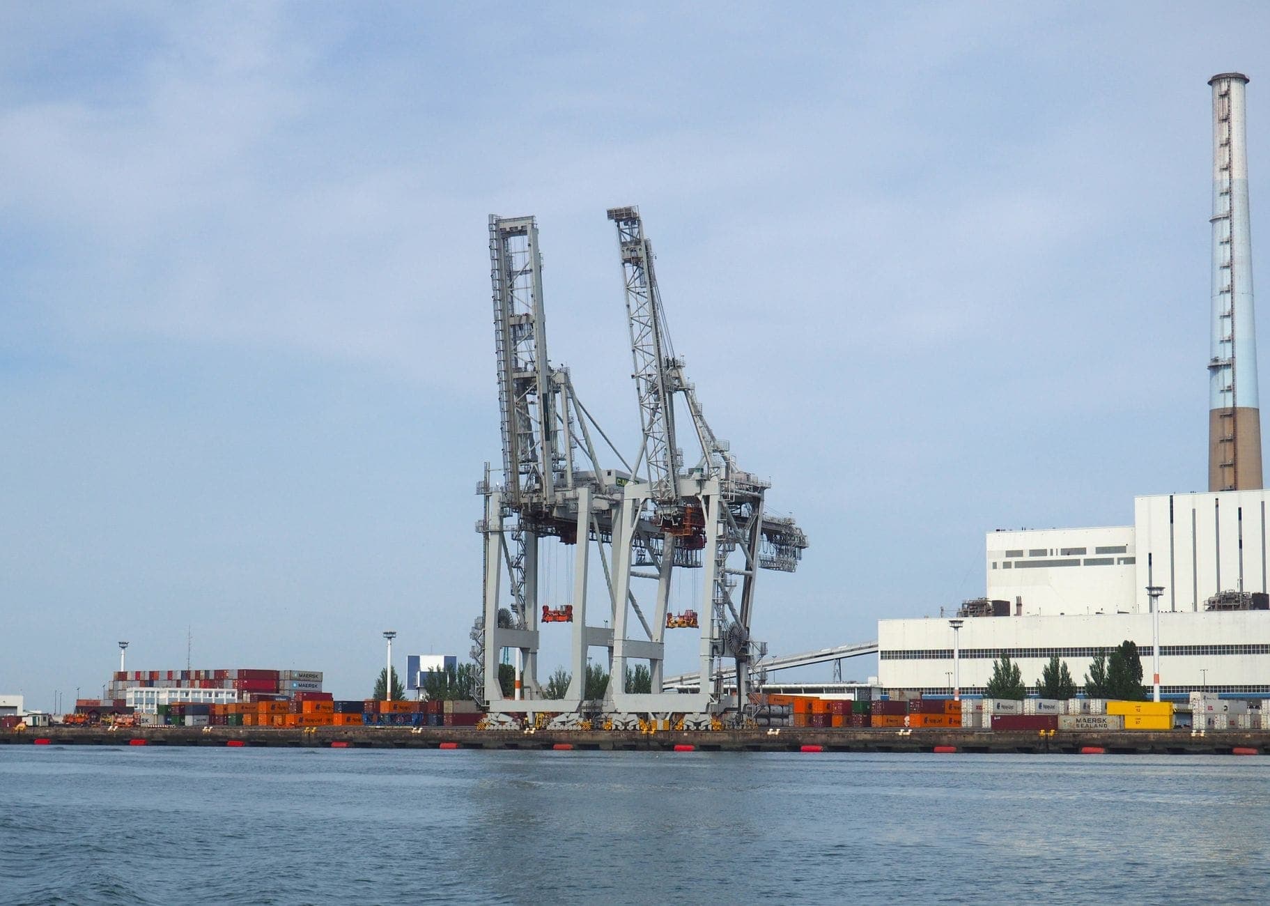 Những cần cẩu cảng khổng lồ và các container hàng hóa xếp chồng lên nhau trải dài dọc bờ kè tại Port of Le Havre dưới bầu trời ban ngày có mây một phần.