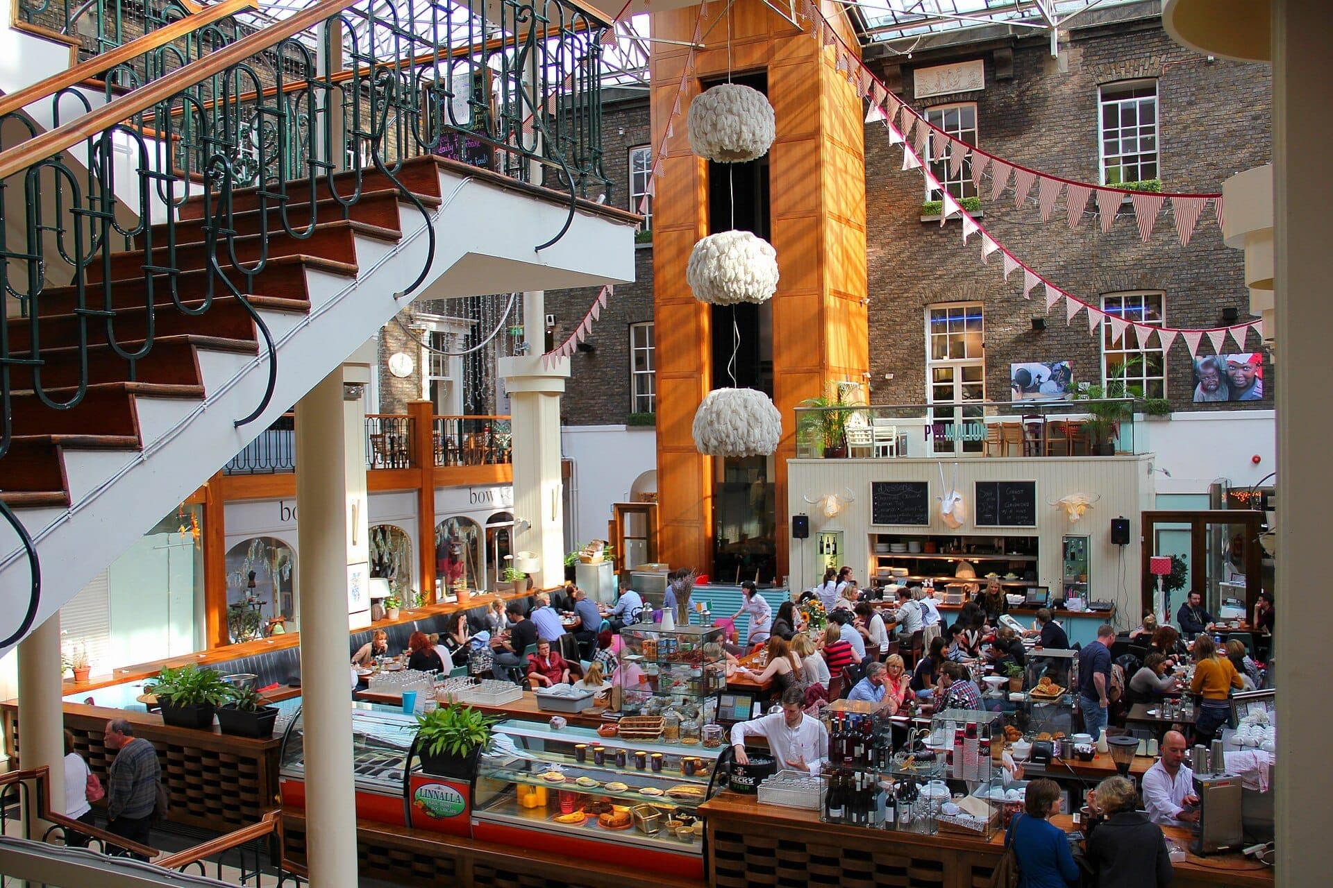Der sonnige Innenhof des Powerscourt Centre beherbergt ein großes, belebtes Café mit Besuchern, umgeben von georgianischen Backsteinmauern, dekorativen Wimpelketten und stilvollen Innentreppen.