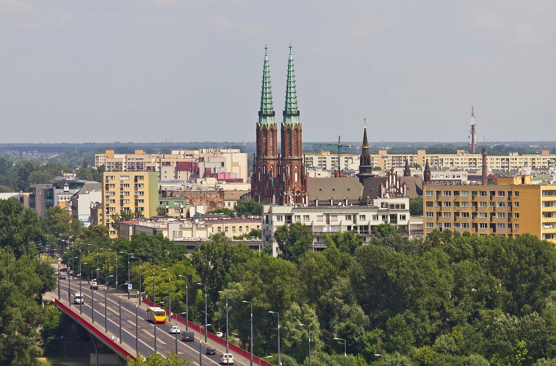 Blick auf das Praga-Viertel in Warschau mit den Doppeltürmen der St.-Florian-Kathedrale zwischen Wohngebäuden und belaubten Bäumen unter einem klaren Himmel.