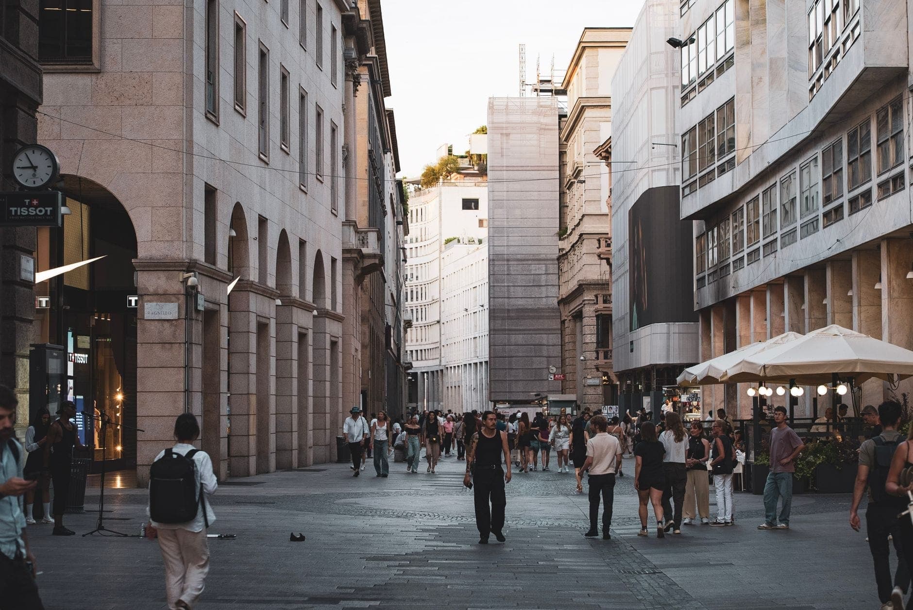Fashionable pedestrians stroll along a stylish, upscale street lined with elegant buildings and high-end boutiques in Milan’s Quadrilatero della Moda district.