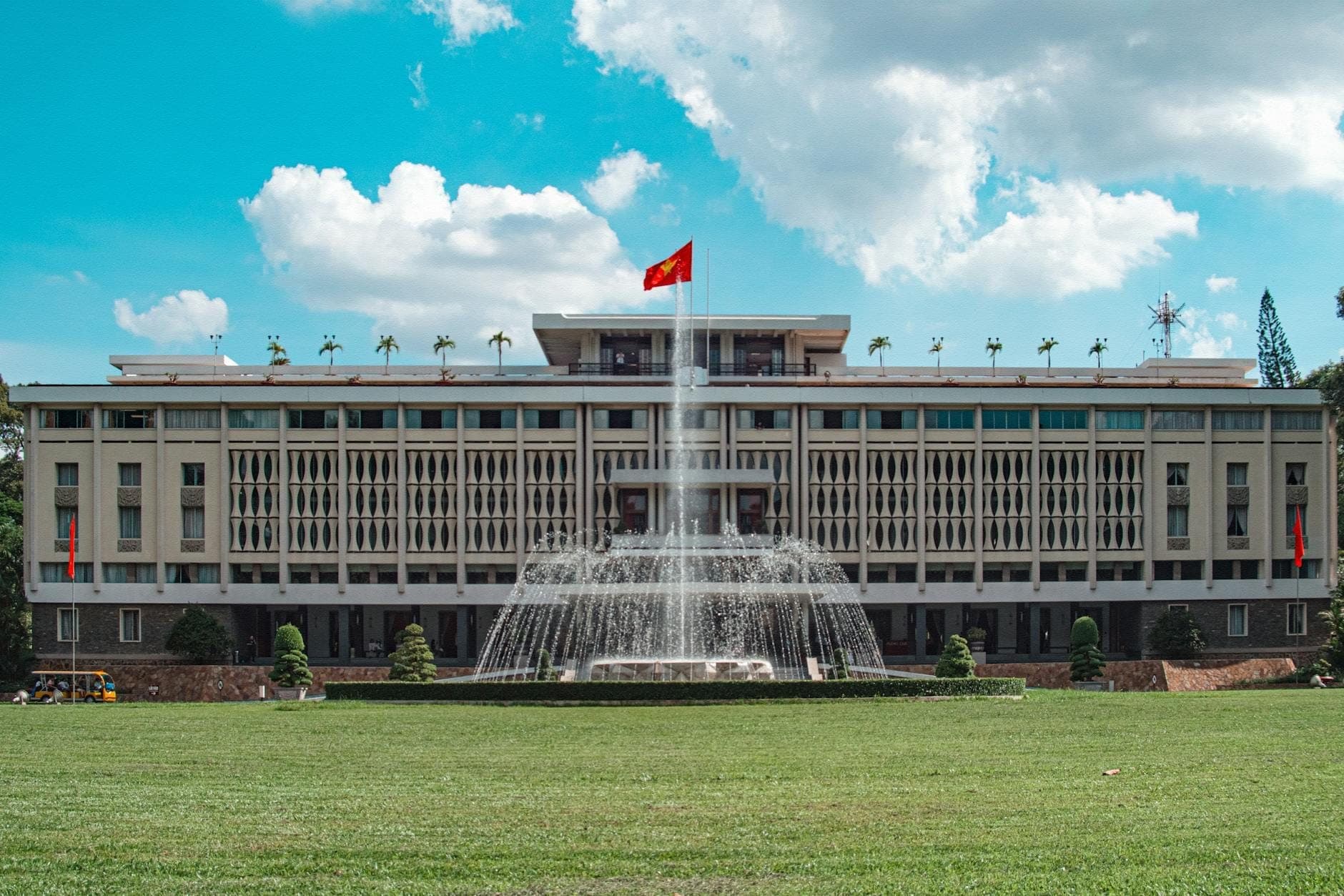 Toàn cảnh đối xứng của Dinh Độc Lập tại TP. Hồ Chí Minh với đài phun nước lớn và cờ Việt Nam tung bay dưới bầu trời xanh trong.