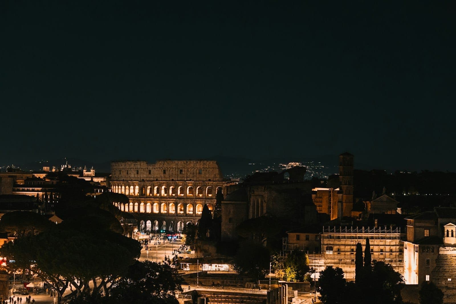 Toàn cảnh Đấu trường La Mã và những con phố Rome lung linh trong đêm, ánh đèn thành phố và các di tích cổ đại sáng rực dưới bầu trời tối.