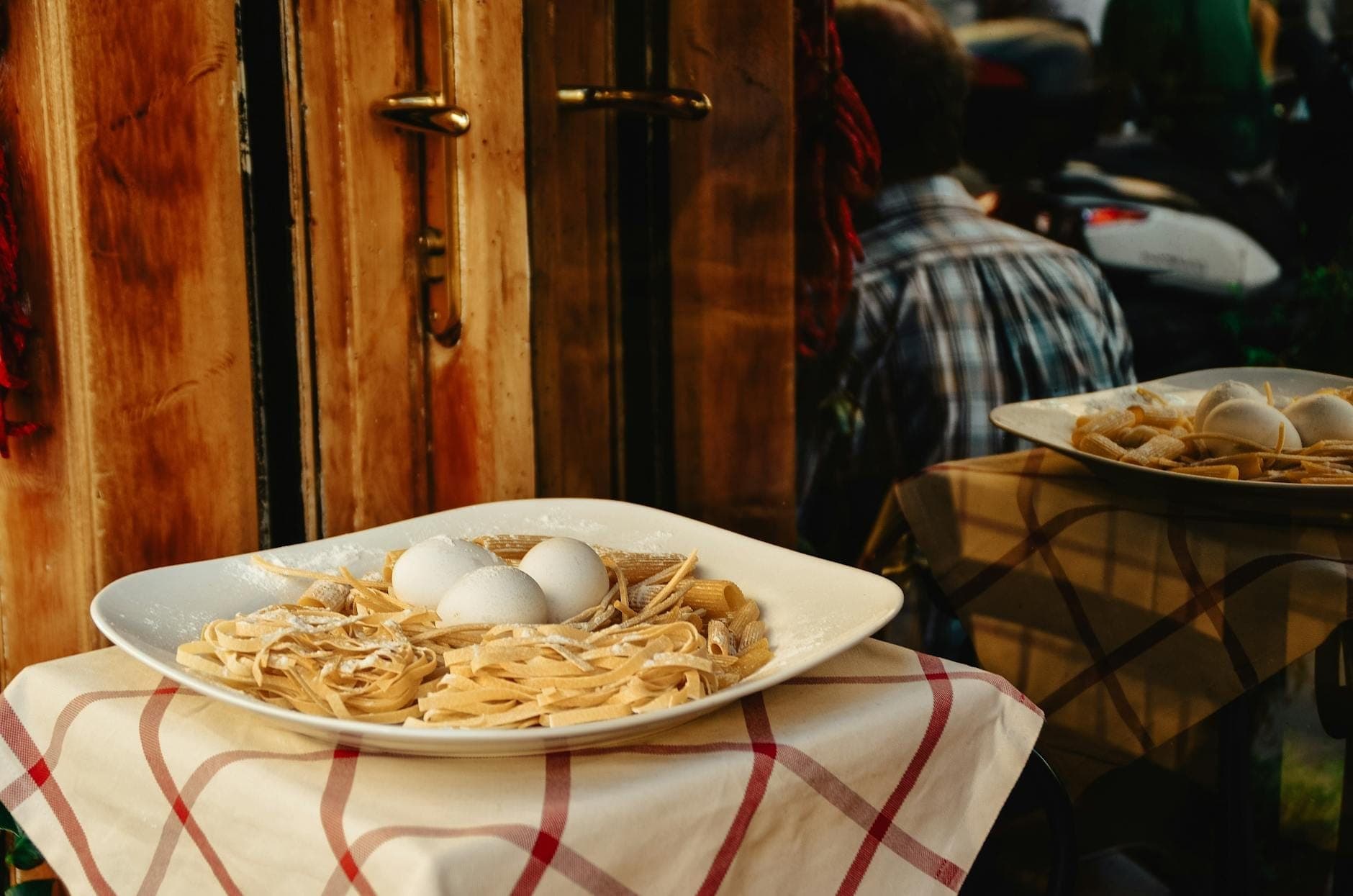 Cận cảnh đĩa carbonara truyền thống kiểu La Mã trên chiếc khăn trải bàn kẻ ca-rô trước một nhà hàng mộc mạc ở Rome.