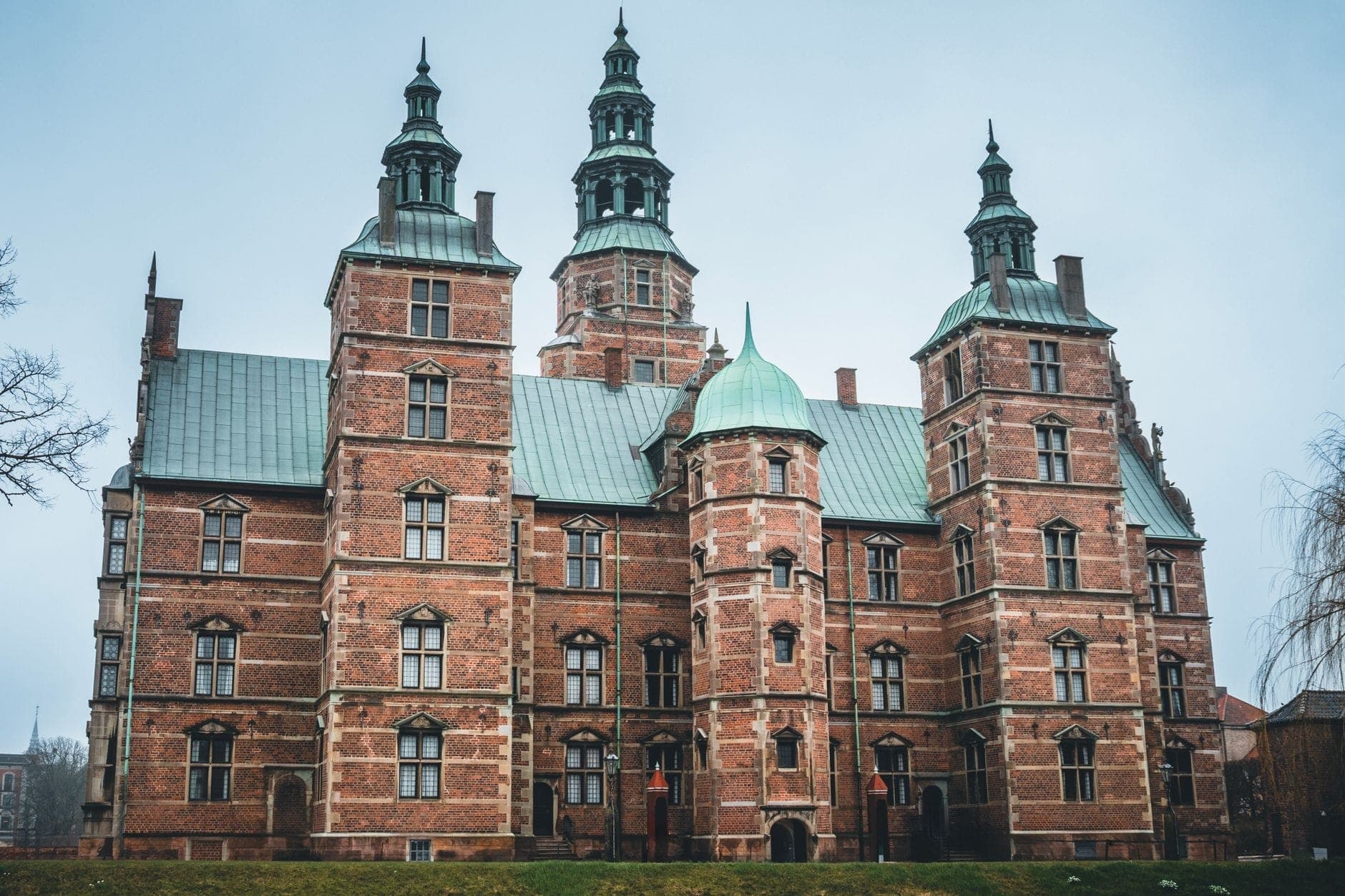 Frontansicht von Schloss Rosenborg in Kopenhagen an einem bewölkten Tag mit seiner roten Backsteinarchitektur im Renaissancestil und den grünen Kupfertürmen.