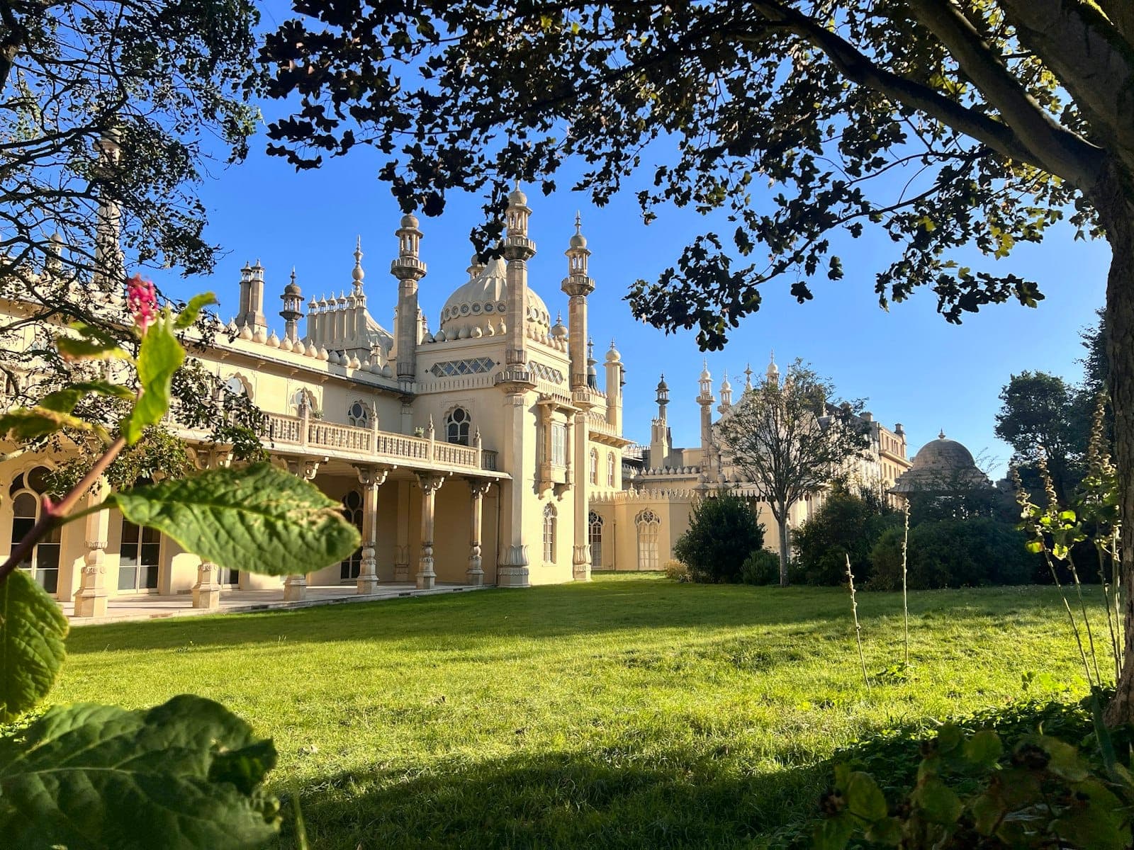 Royal Pavilion ở Brighton nhìn qua tán cây xanh, nổi bật giữa khu vườn Regency rực rỡ và bầu trời xanh trong.