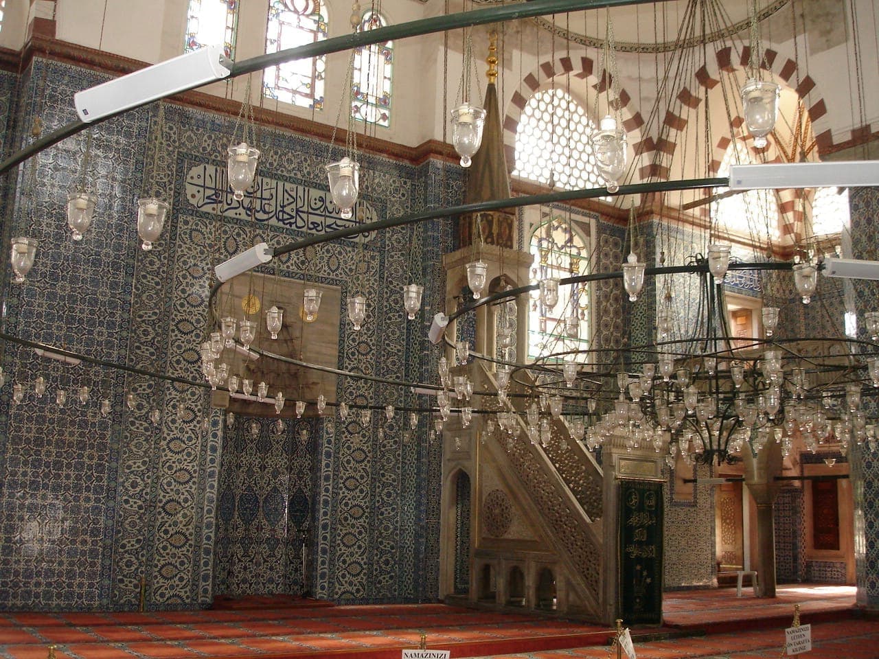 Das Innere der Rüstem-Paşa-Moschee zeigt Wände, die mit aufwendigen blauen Iznik-Fliesen bedeckt sind, bogenförmige Buntglasfenster und einen großen zentralen Kronleuchter.