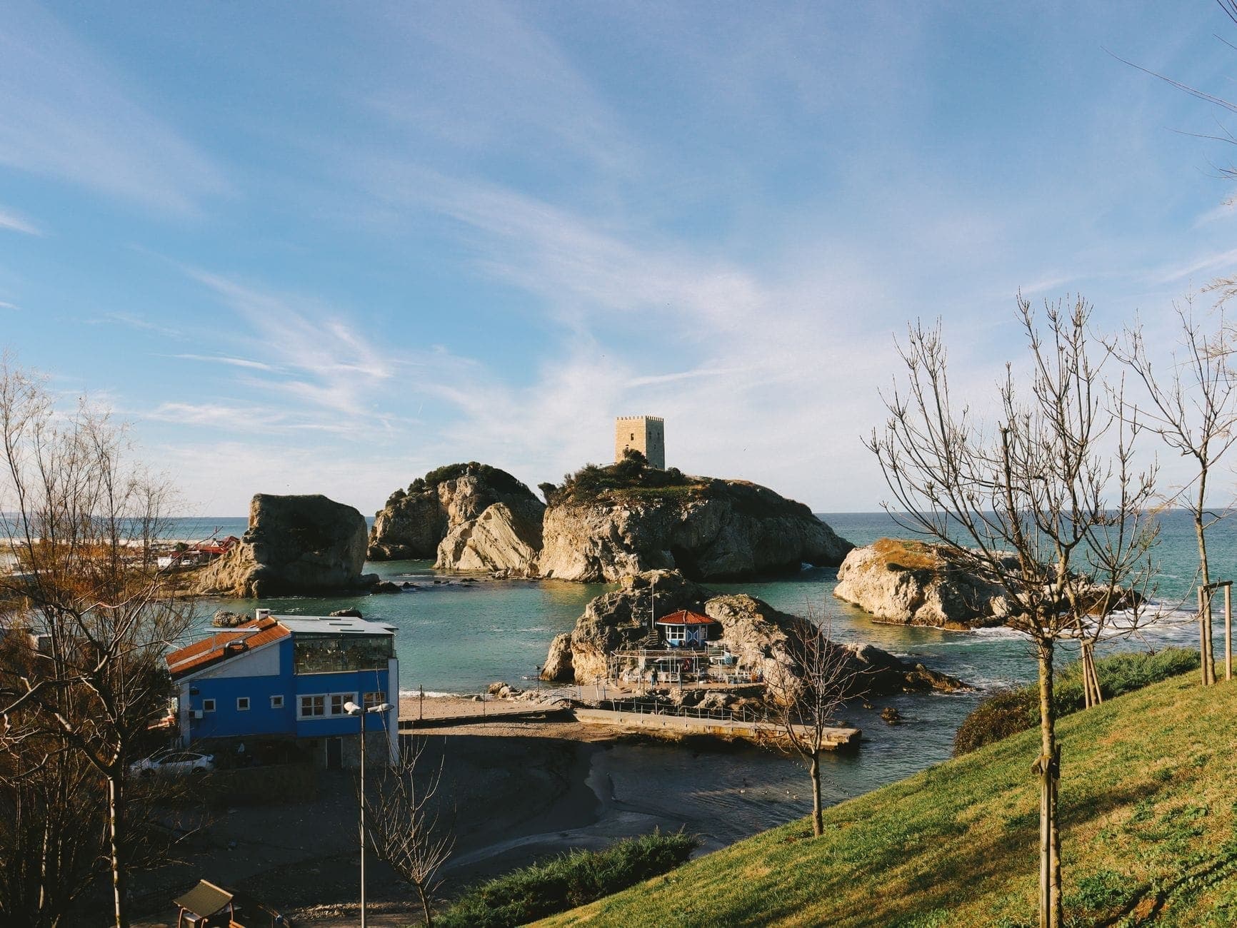 Felseiland mit einer mittelalterlichen genuesischen Burg, umgeben von türkisfarbenem Schwarzmeerwasser unter hellem Himmel, von einem Grashügel mit Küstengebäuden aus fotografiert.