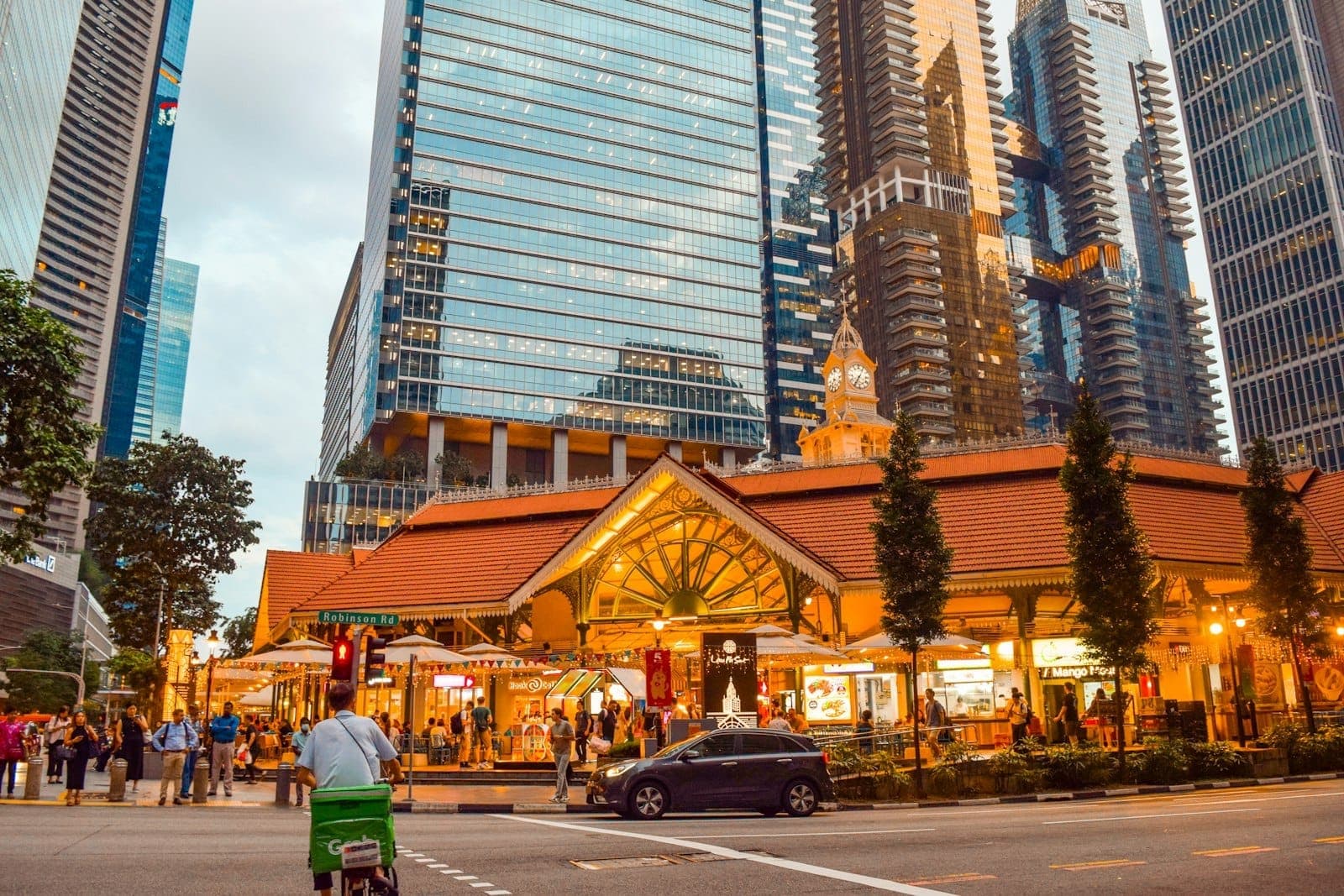 Evening view of Lau Pa Sat hawker centre with people outside, surrounded by modern skyscrapers and city lights in Singapore’s downtown core.
