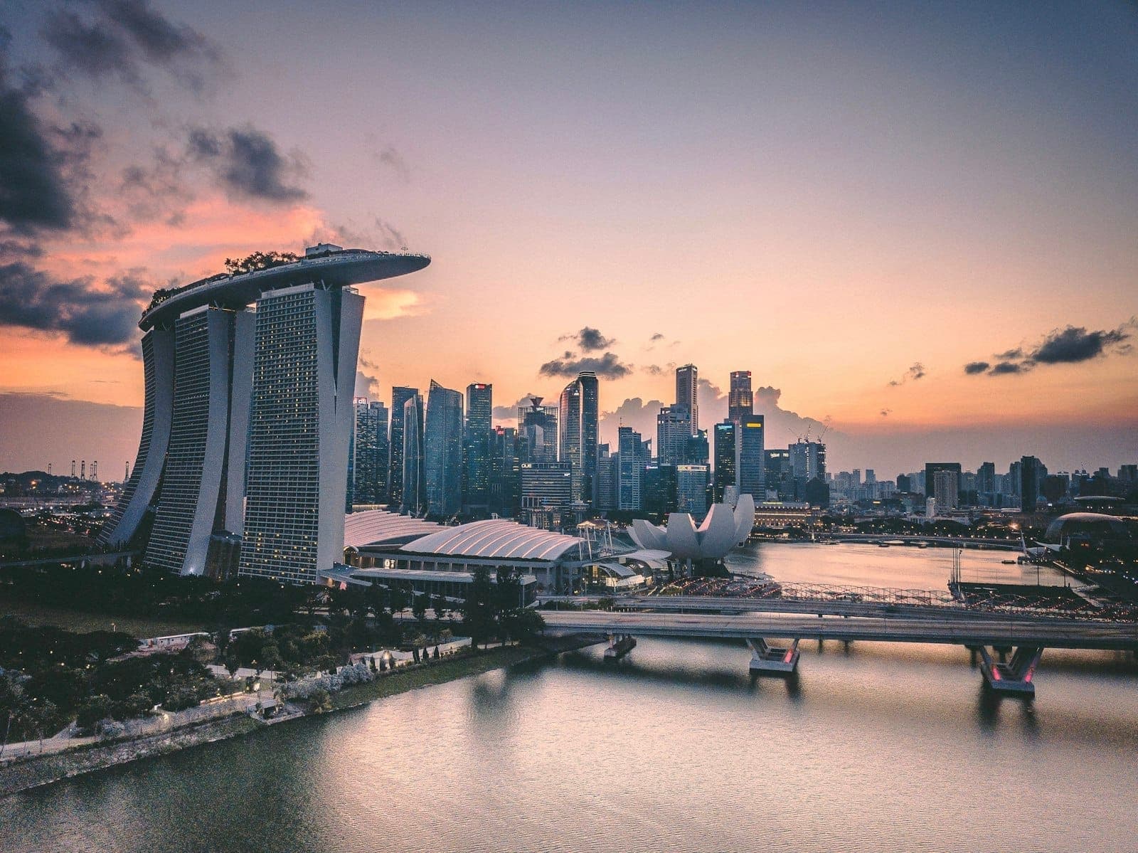 Marina Bay Sands hotel and Singapore city skyline at sunset, with illuminated clouds and calm water in the foreground.