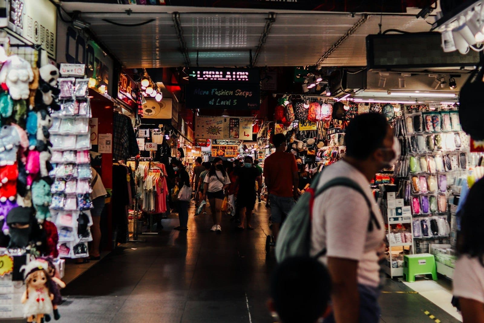 Indoor market scene with busy walkways, budget clothing, accessories, souvenirs, and shoppers at stalls, typical of Singapore's bargain shopping spots.