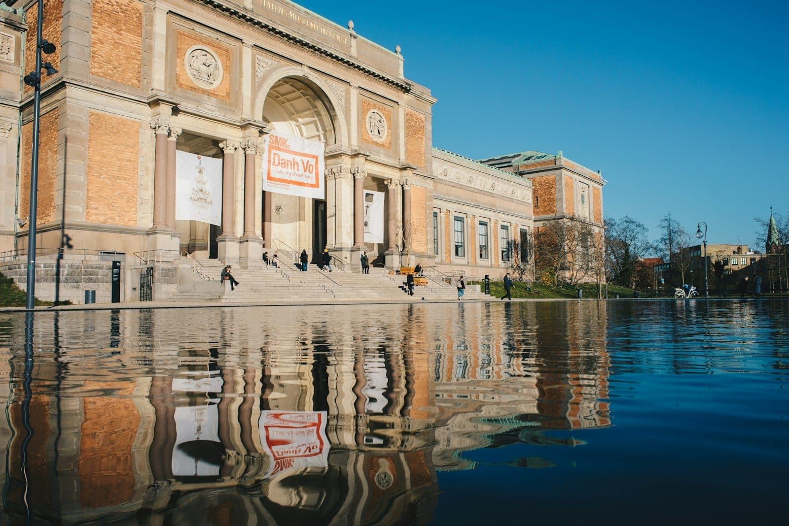 Hauptfassade des SMK – Statens Museum for Kunst in Dänemark, mit großer Freitreppe, Spiegelbecken und Besuchern unter klarem blauen Himmel.