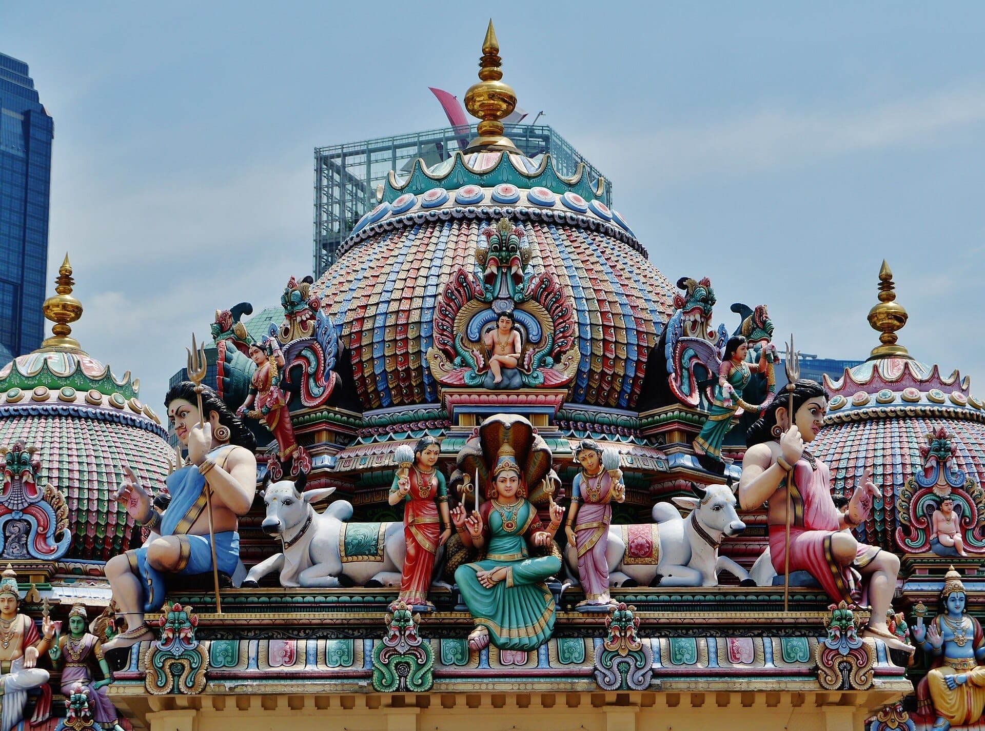 Intricate, colorful statues and carvings adorn the domed rooftop of Sri Mariamman Temple under a bright blue sky in Singapore’s Chinatown.