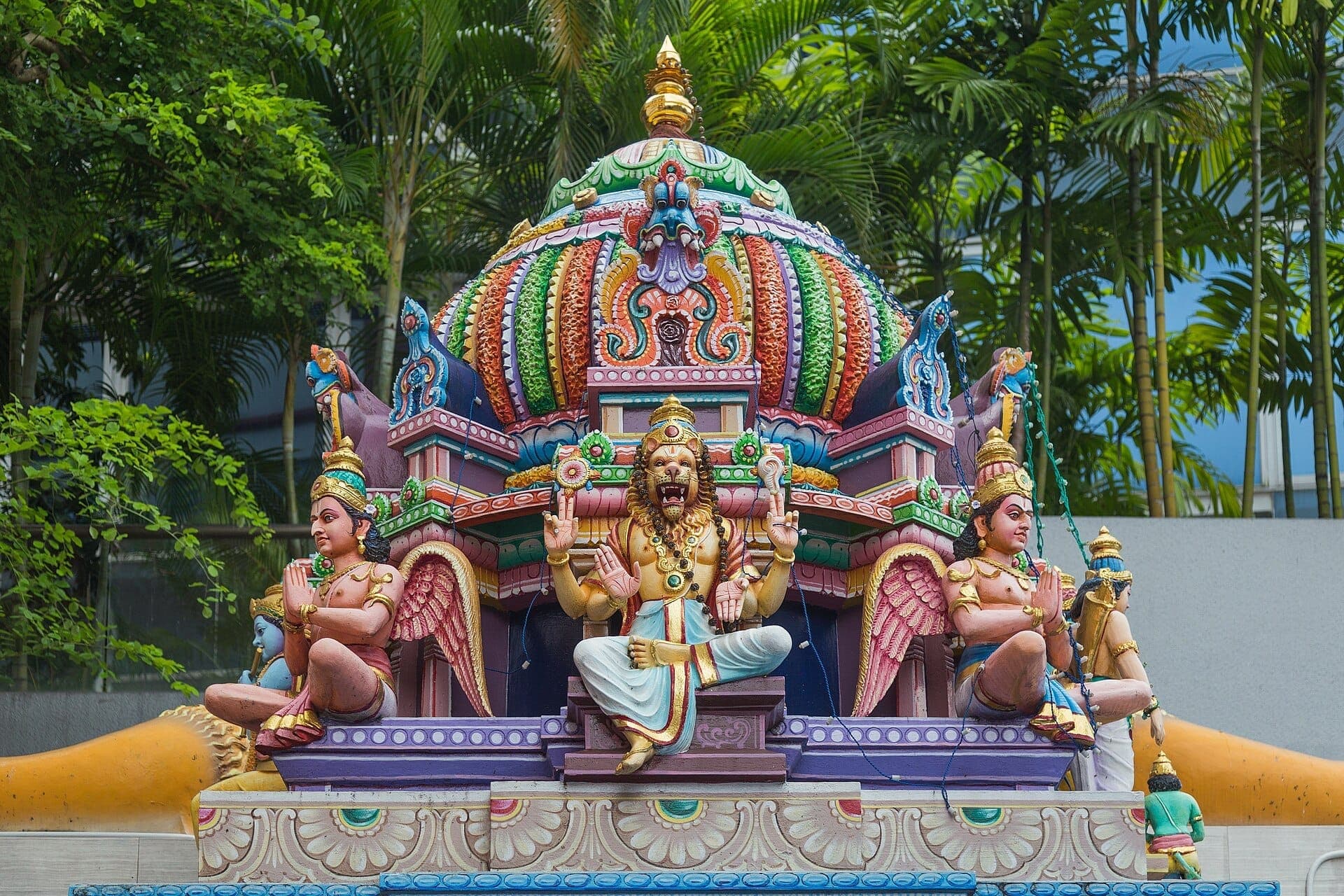 Colorful stucco statues and ornate dome detail on the Sri Veeramakaliamman Temple, framed by tall green palms under natural daylight.