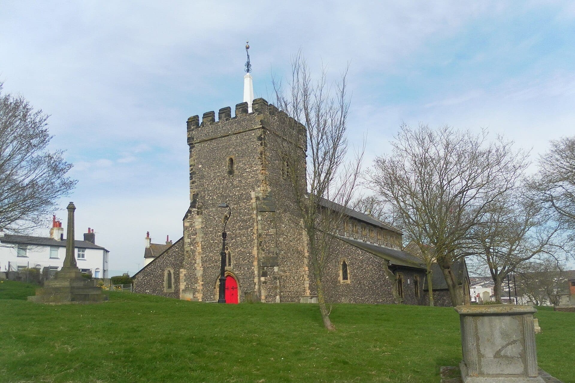 Nhà thờ St Nicholas of Myra ở Brighton, một tòa nhà đá cổ kính với tháp có lỗ châu mai và cửa màu đỏ, bao quanh bởi sân nhà thờ có cỏ và những cây trụi lá.