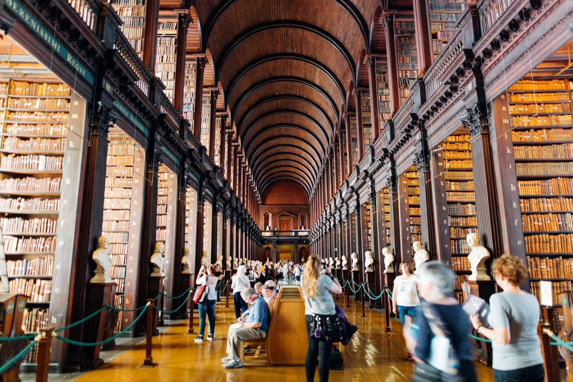 Innenraum der Bibliothek des Trinity College in Dublin mit Bögen, Bücherregalen und Besuchern, die das historische Wahrzeichen erkunden.