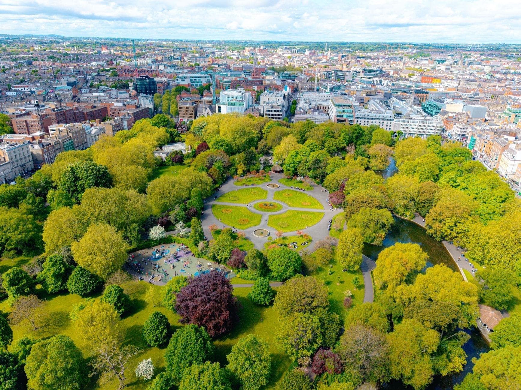 Vista aérea de St Stephen's Green en el centro de Dublín, con frondosos árboles, senderos circulares y el paisaje urbano que rodea el parque.