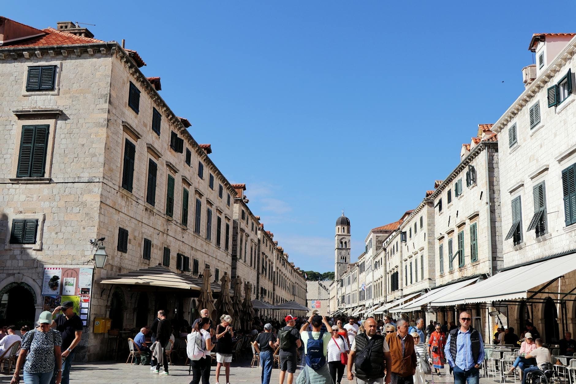 Đại lộ Stradun trong Phố Cổ Dubrovnik đông đúc người qua lại, hai bên là những tòa nhà đá vôi và bầu trời xanh trong vắt phía trên.