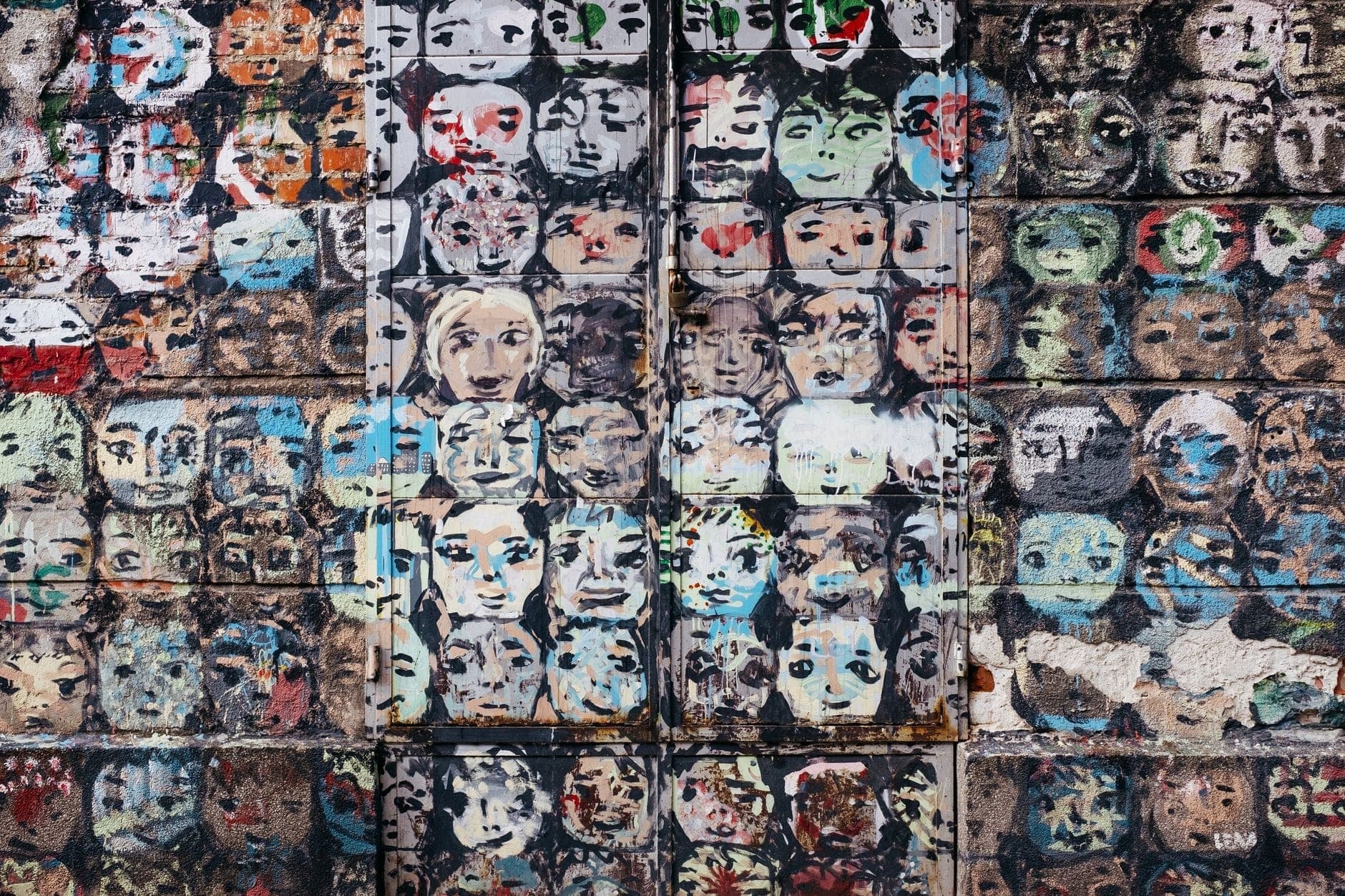 Bunte Wand, übersät mit dutzenden geschablonten Gesichtern in verschiedenen Stilen und Farben – Street Art im Warschauer Viertel Praga.